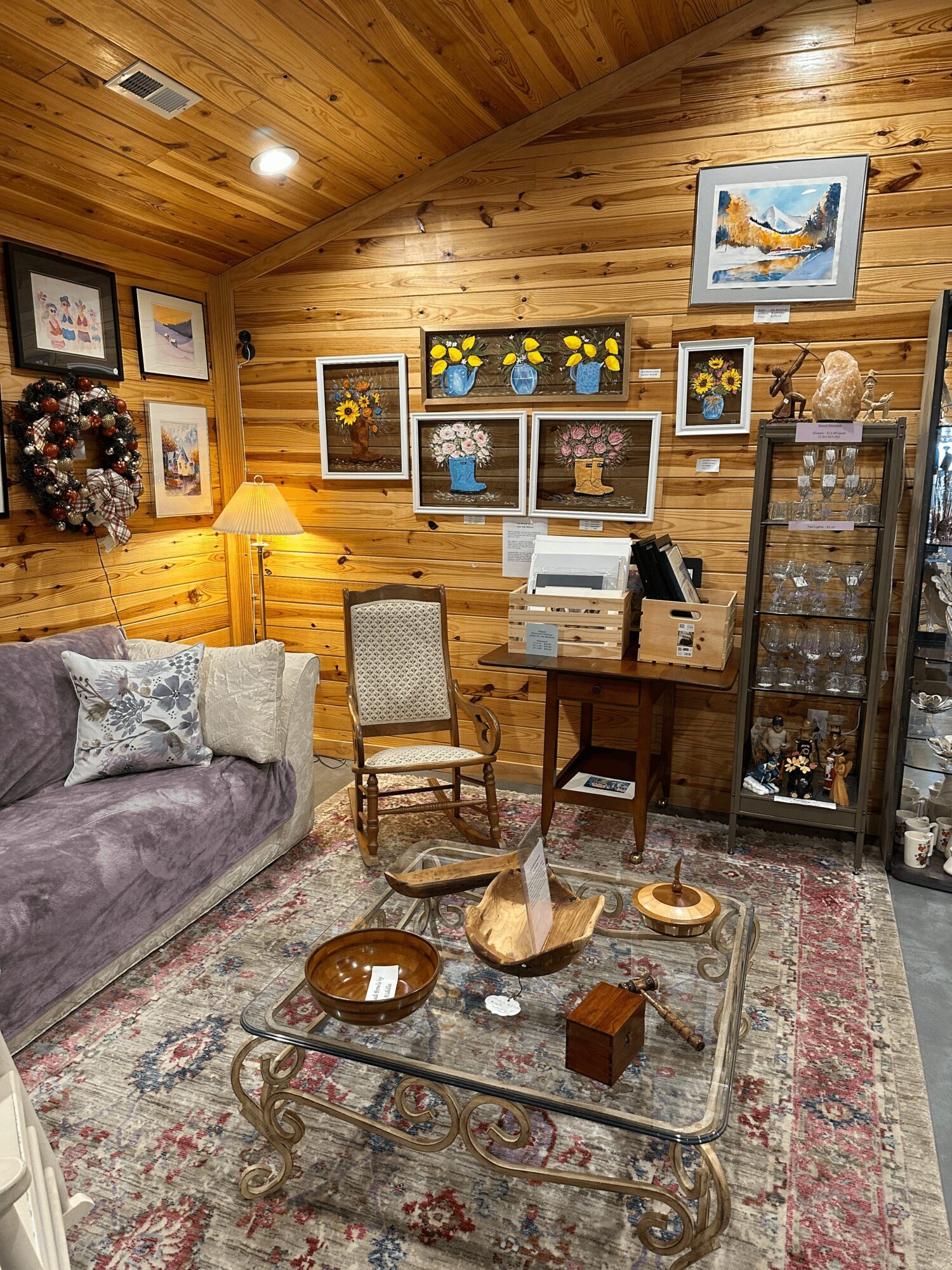 Cozy room with wooden walls, framed artwork, a sofa with pillows, a glass coffee table, and a display cabinet.