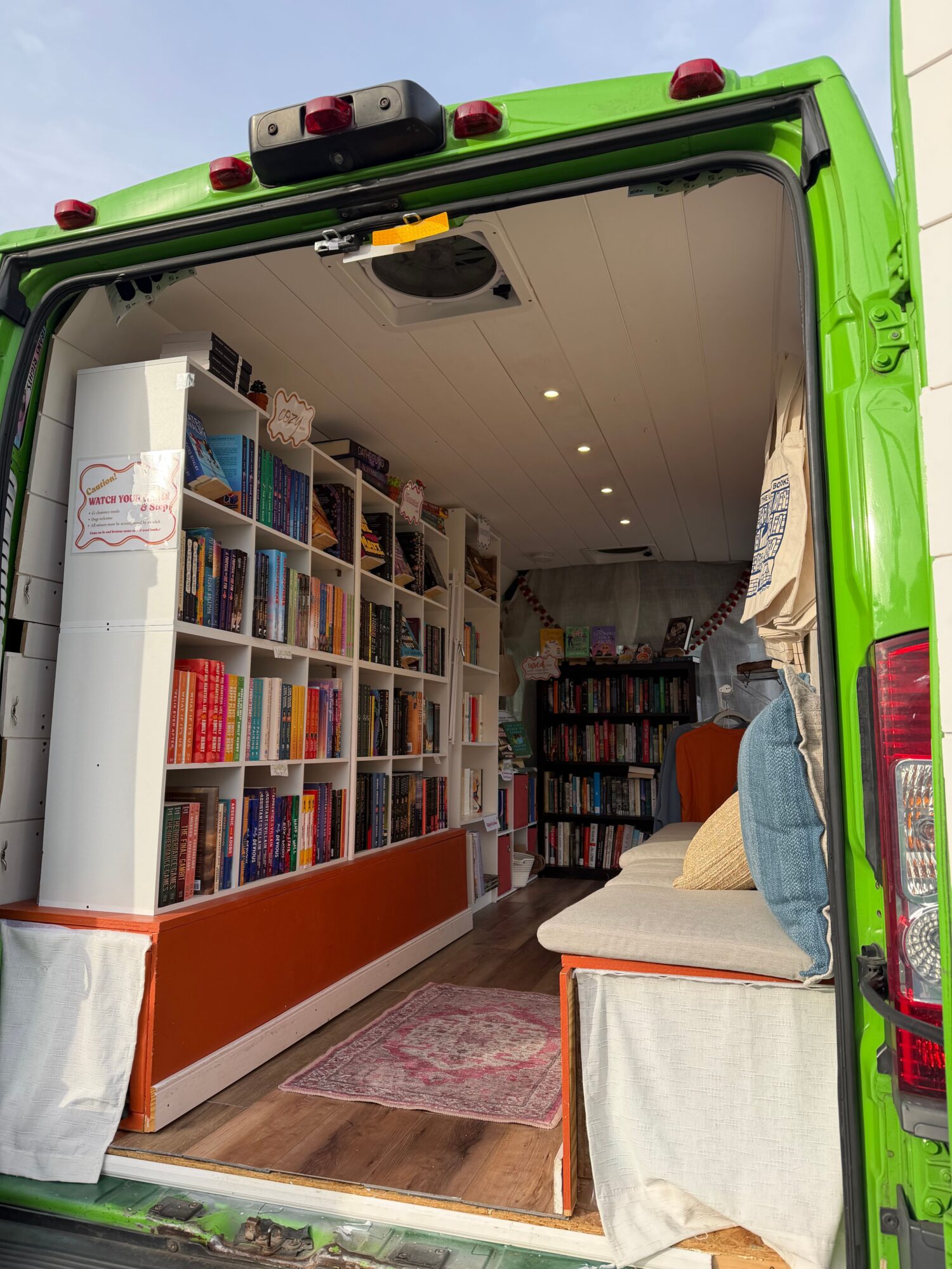 Bookshelves filled with books inside a green vehicle, with a table and a curtain visible.
