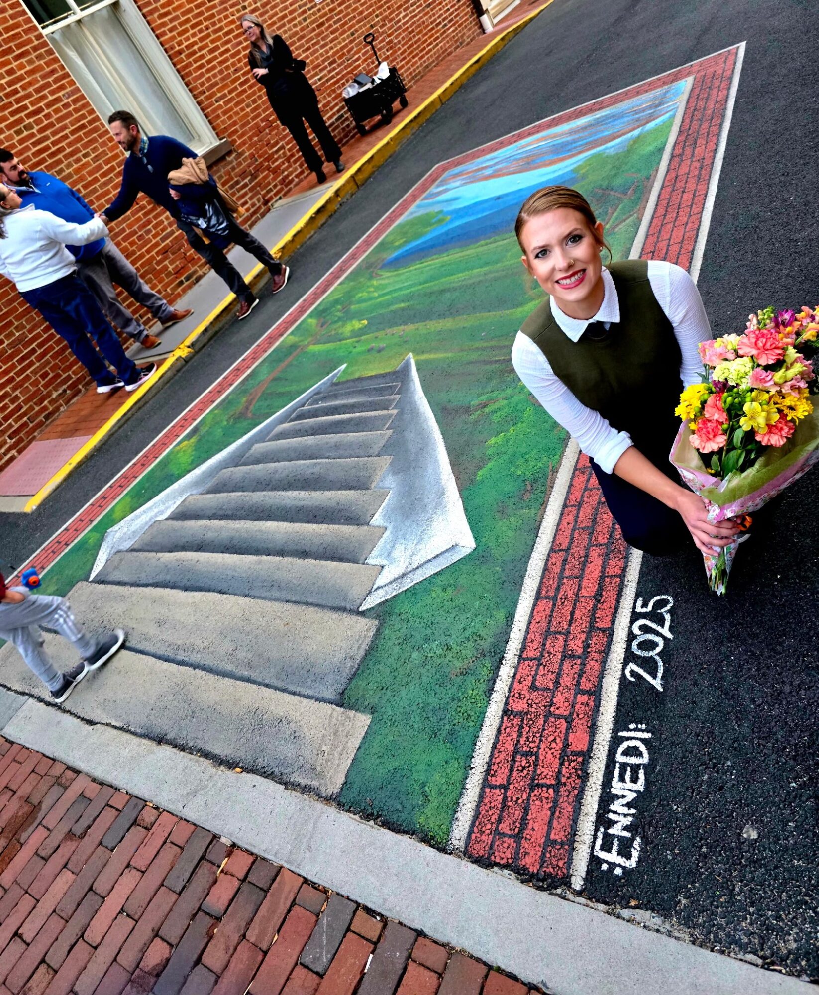 Girl holding a bouquet of flowers on a colorful chalk art sidewalk, with stairs and people in the background.