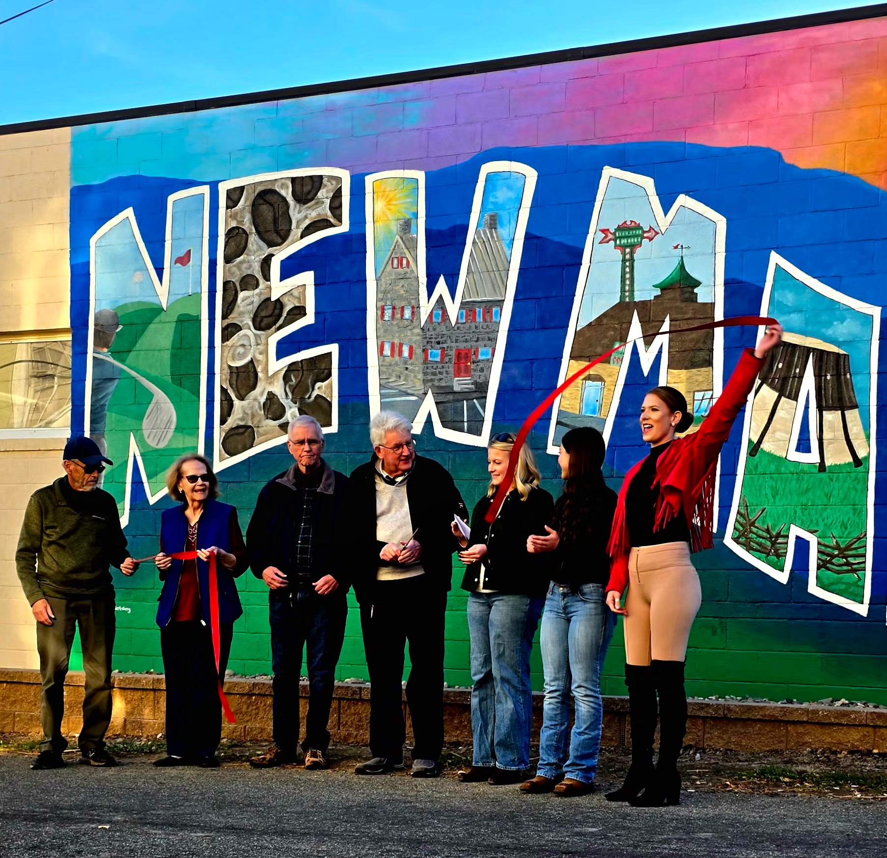 Group of seven people standing in front of a colorful mural with large letters spelling 'NEW'.