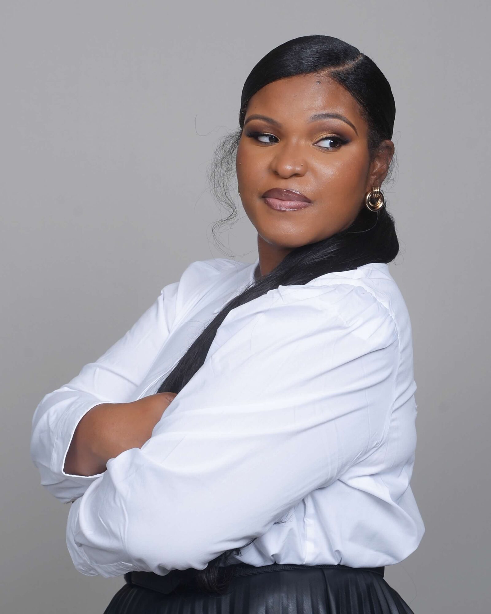 Woman with crossed arms, wearing a white shirt, looking to the side, against a plain background.
