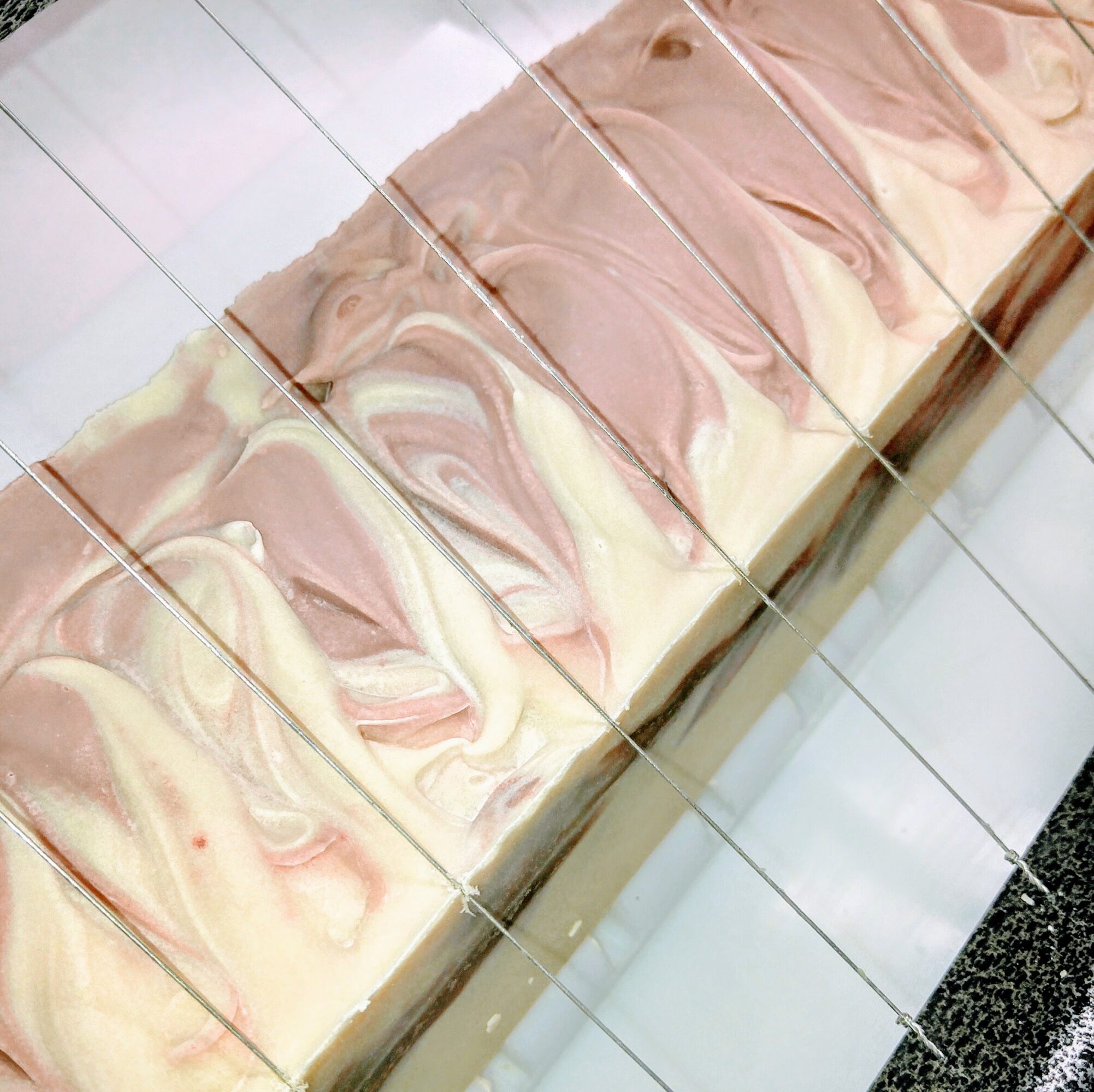 Marbled soap bars with pink, cream, and brown swirls on a white tiled surface.