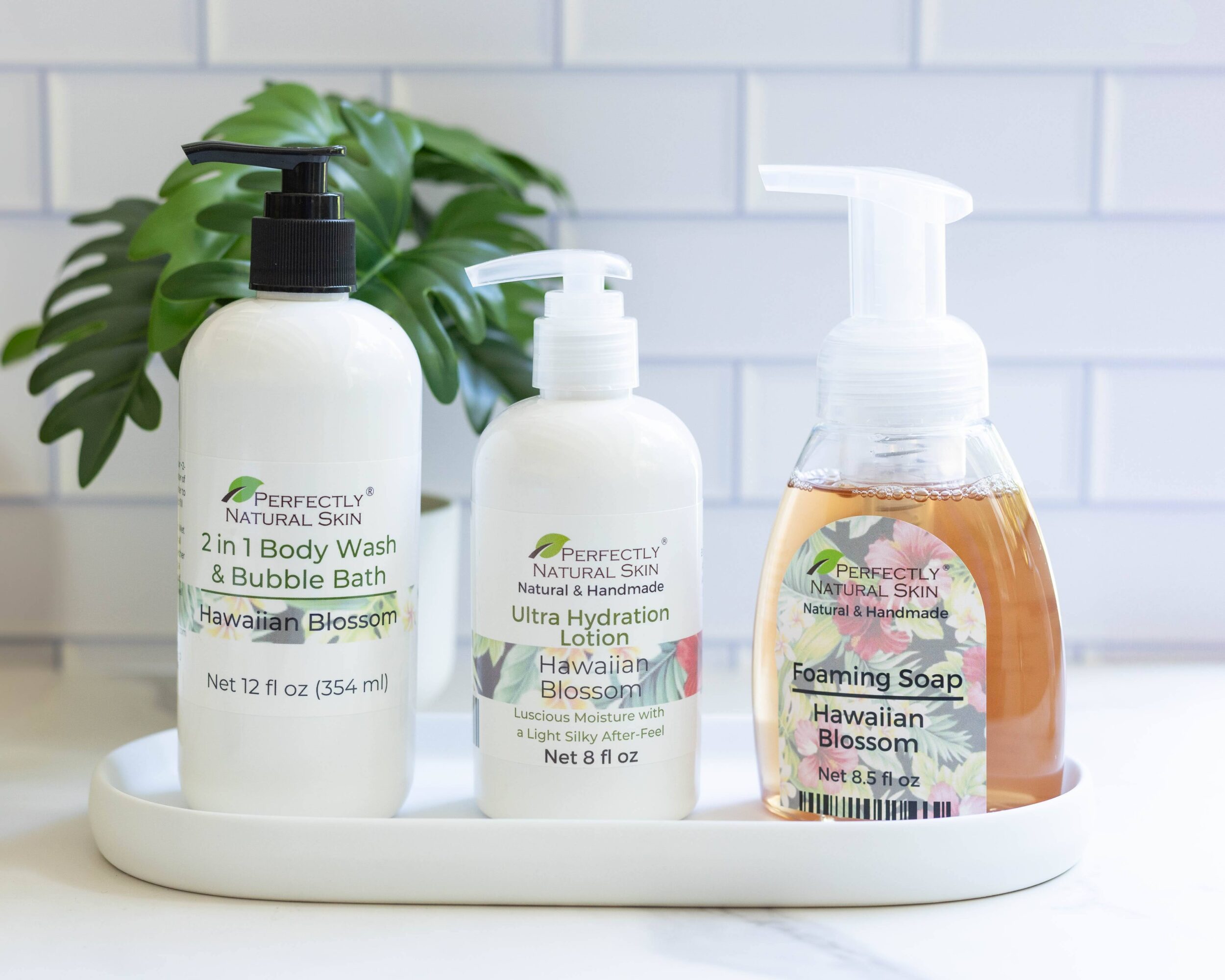 Three bottles of skincare products on a tray with a green plant in the background, against a white tiled wall.