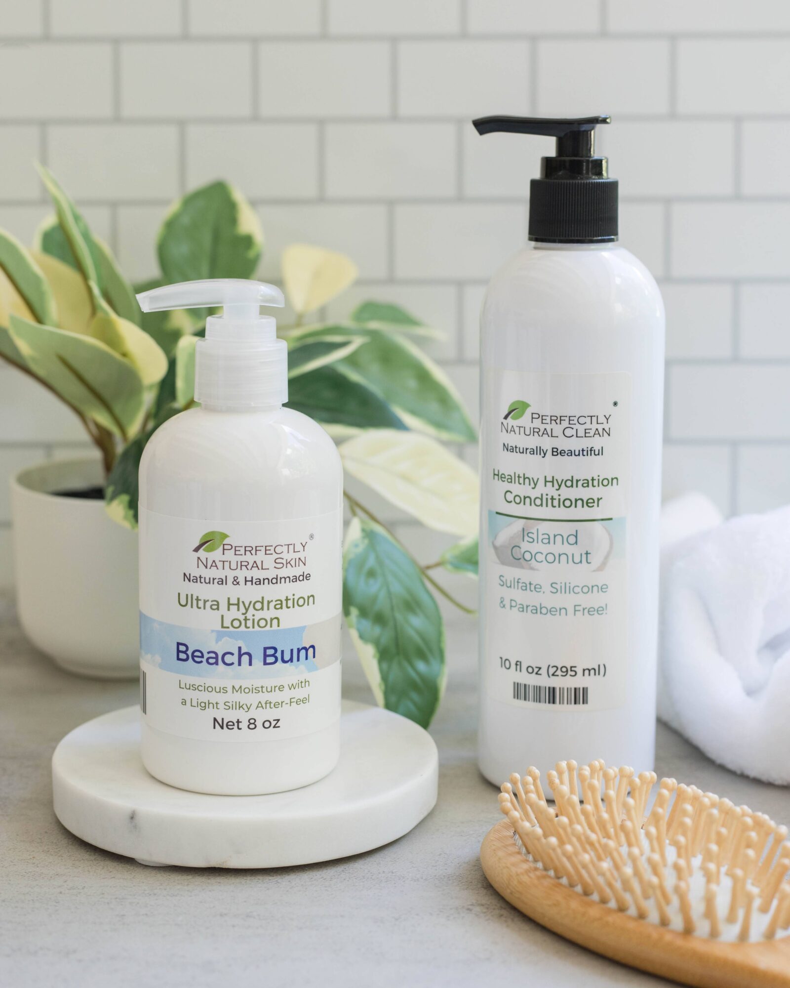 Two bottles of hair care products on a white surface with a plant and a towel in the background.