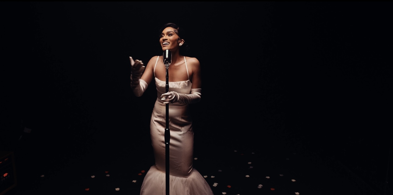 A woman in a strapless gown singing into a microphone on a dark stage.