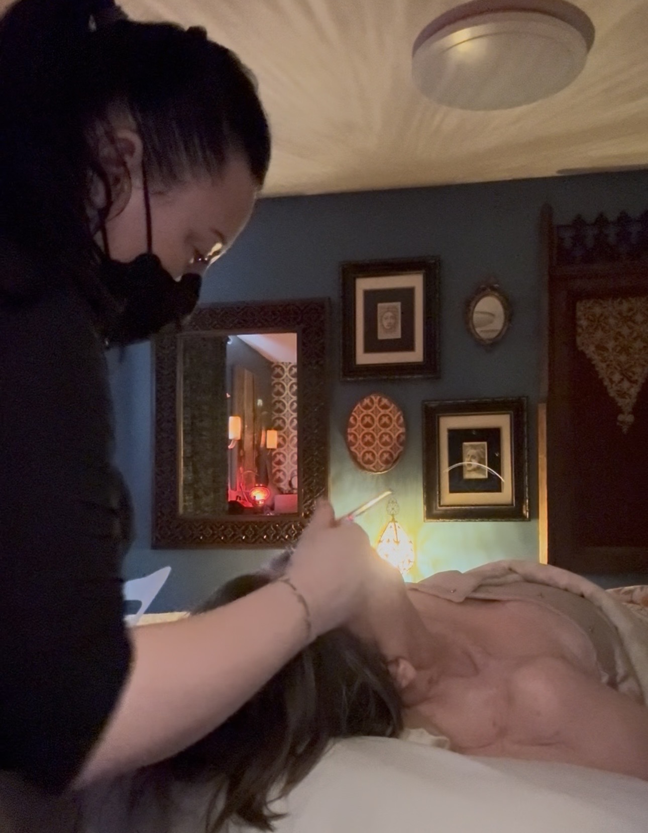 Person wearing a mask appears to be performing a procedure on a person lying in bed in a decorated room.