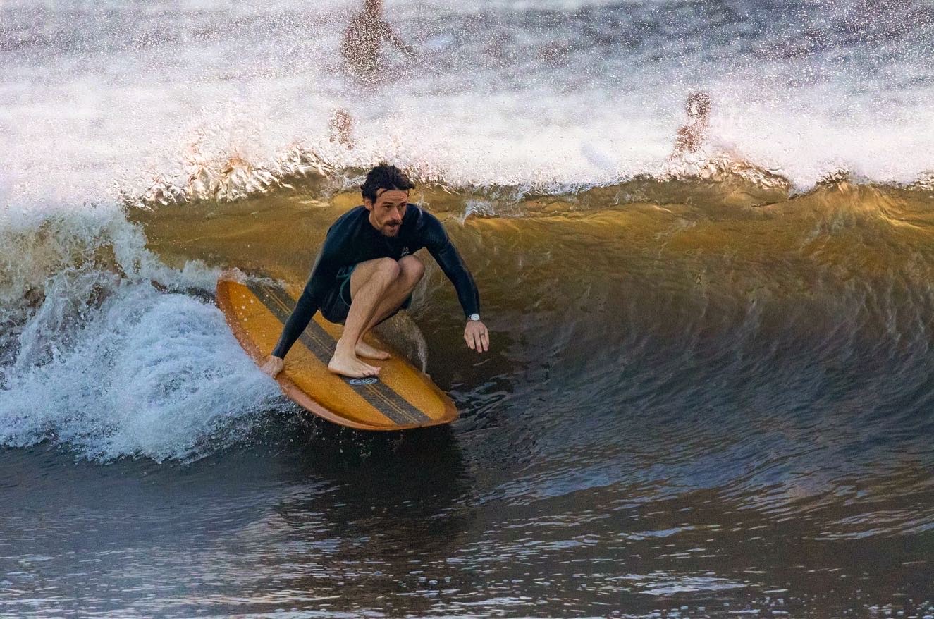 Person surfing on a wave, crouched on a yellow surfboard, with water splashing around.