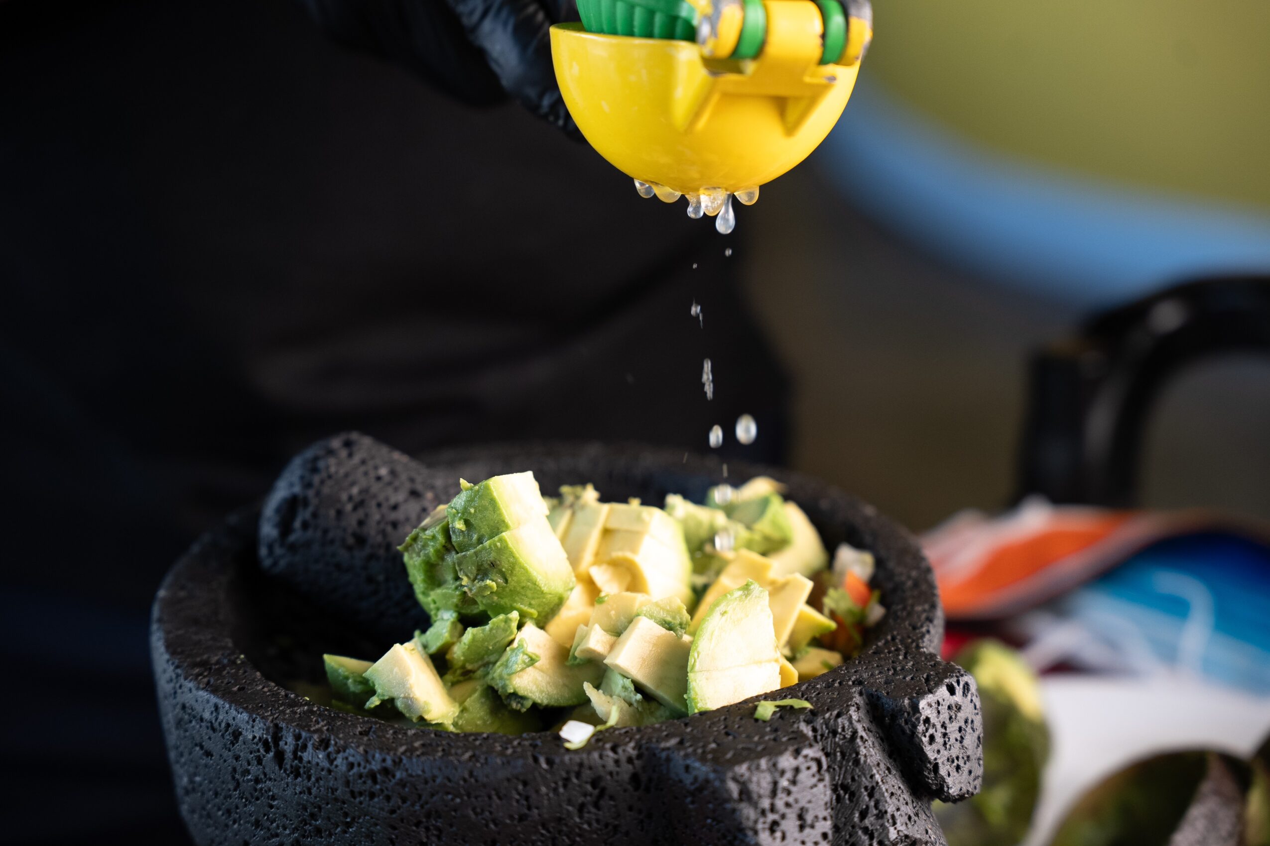 Person grating cucumber into a bowl with a black stone mortar and pestle, salt and water droplets visible.