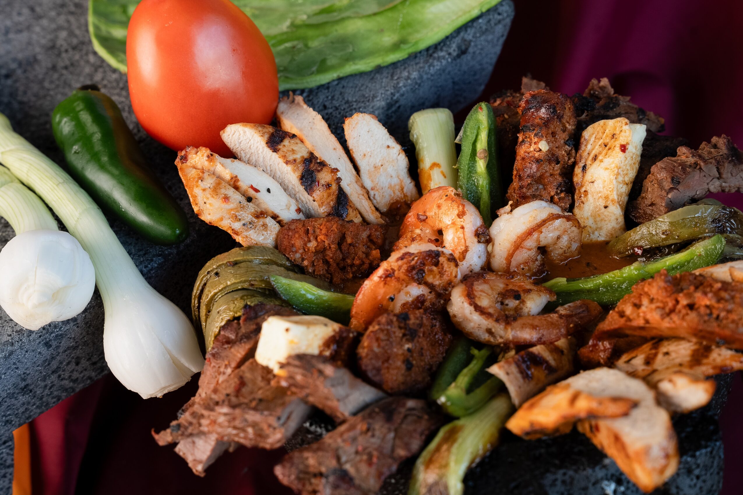 Assorted grilled meats, vegetables, and greens arranged on a platter with tomato, green peppers, and onions.
