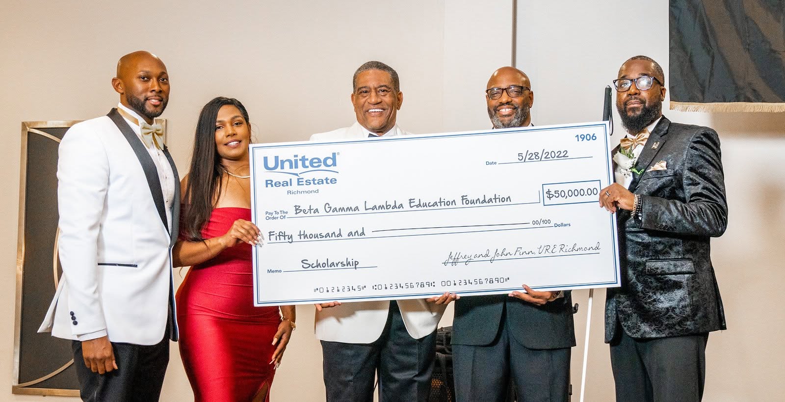 Five people holding a large check, smiling, in a room with a painting on the wall.