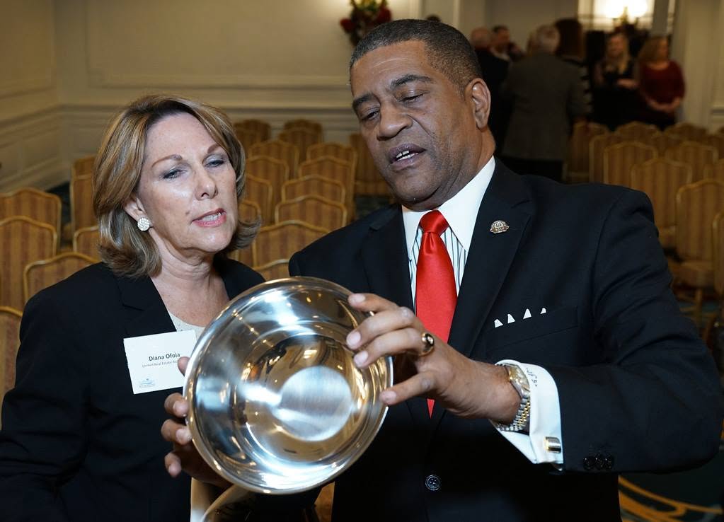 Two people, a woman and a man, look at a shiny, reflective bowl held between them in a formal setting.