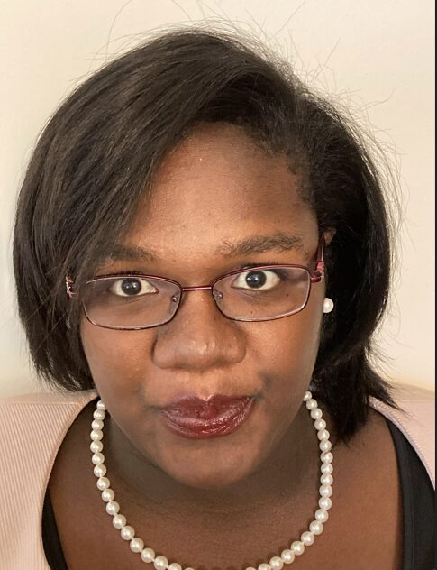 Woman with glasses and pearl necklace looking at camera, neutral background