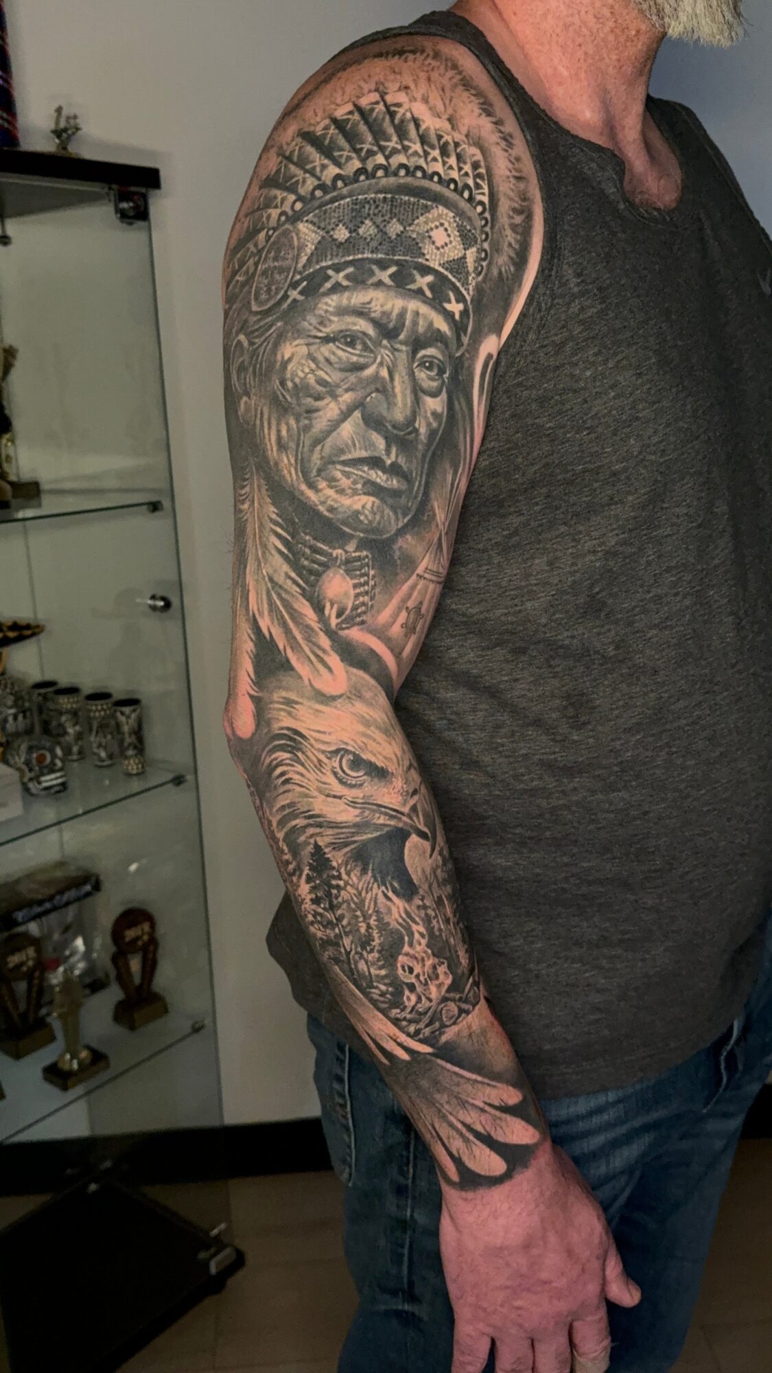 Tattoo of a Native American chief with a headdress on the upper arm, and a wolf on the forearm, detailed black and gray shading.