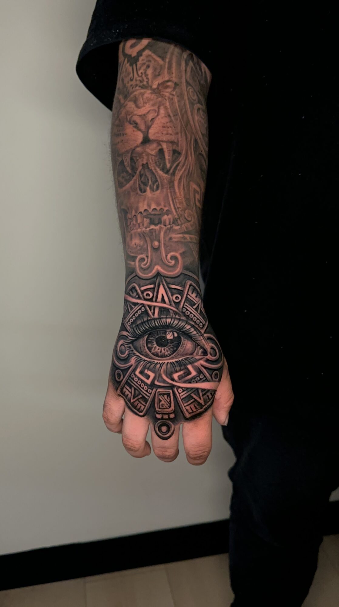 Tattooed arm with detailed black ink designs extending from wrist to elbow, including geometric patterns and symbols.