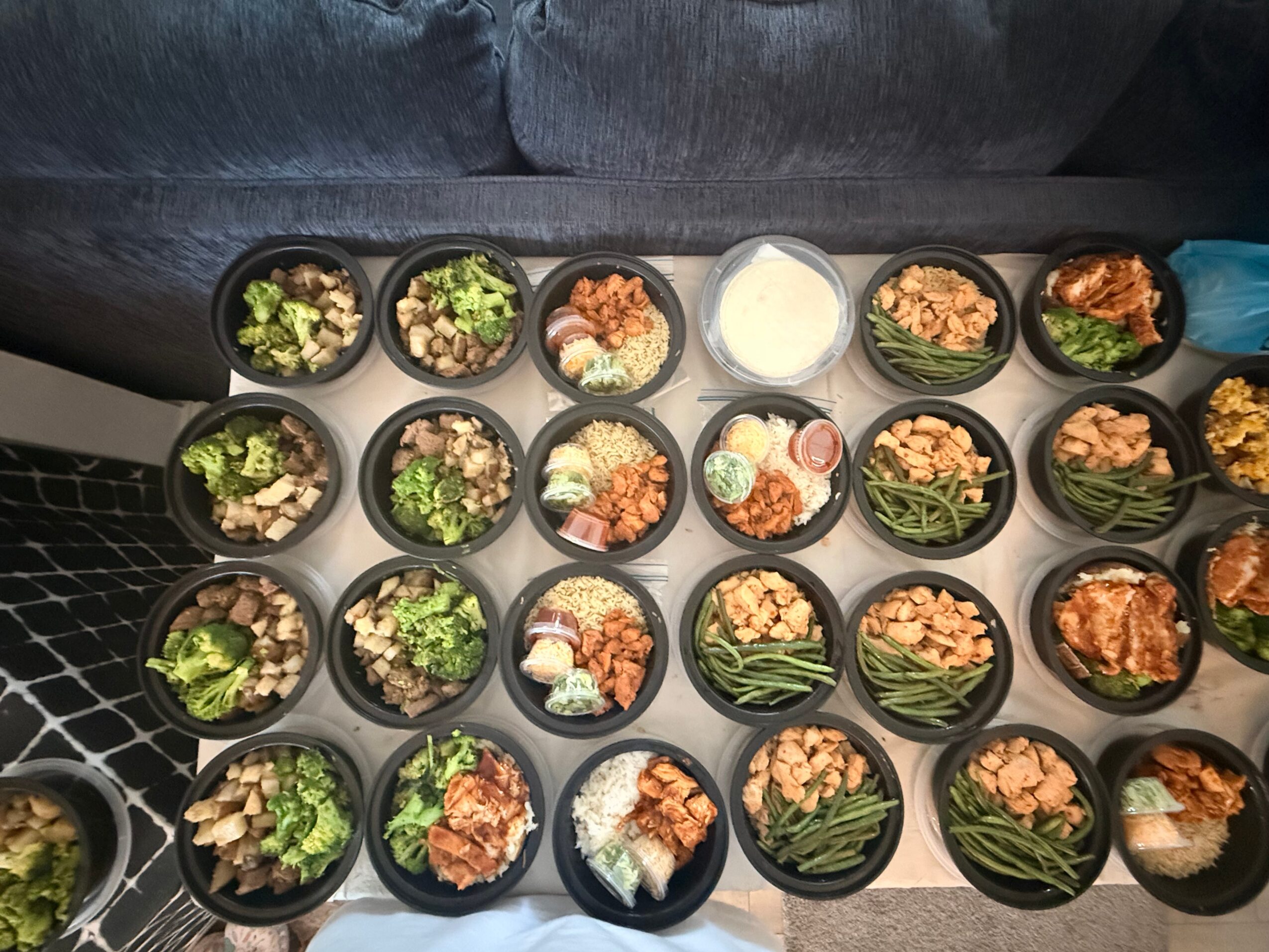 Tray of small bowls with various foods, including vegetables, meats, and sauces, on a table. A blue cup is visible on the right.