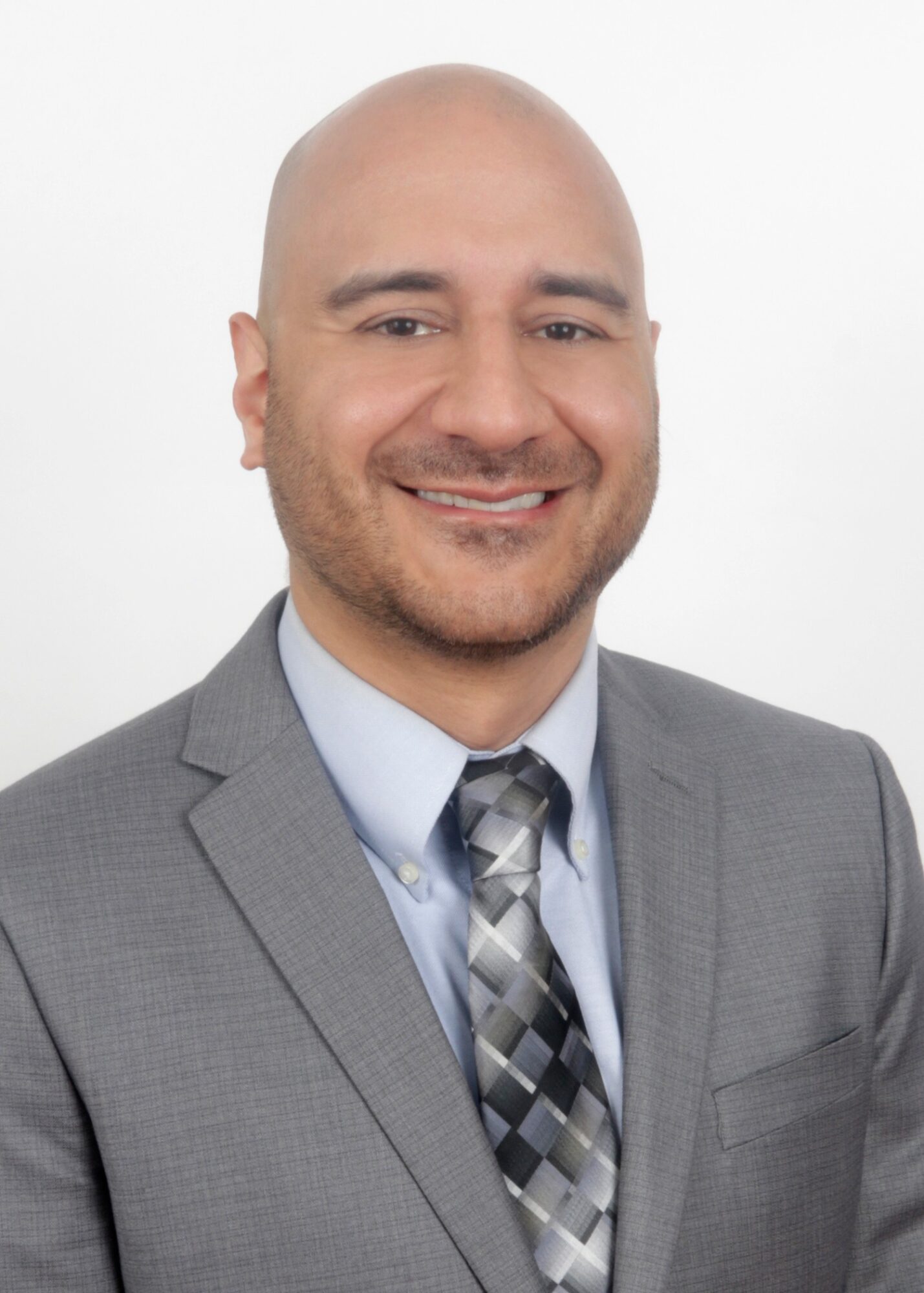 Bald man in gray suit and patterned tie smiling against a white background.
