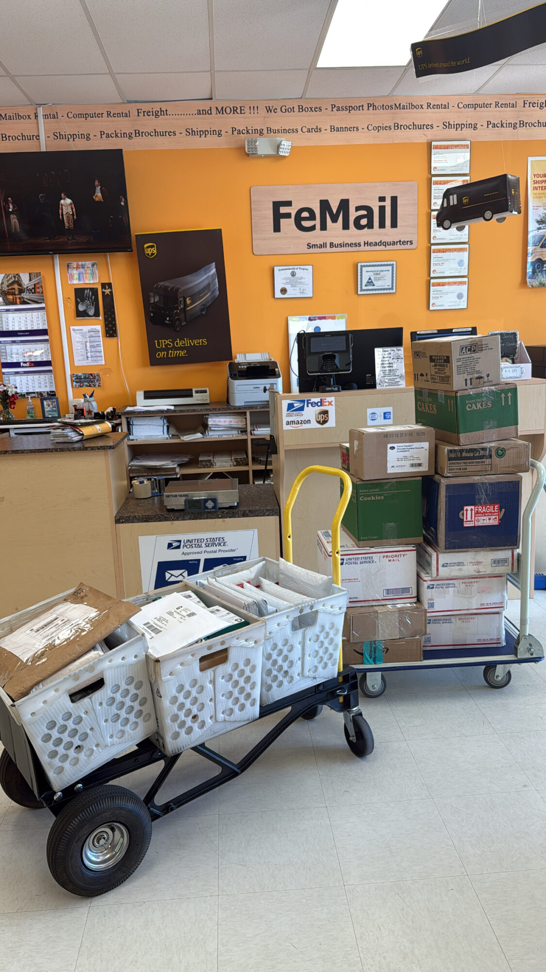 Shopping cart filled with packages and boxes in a store with orange walls and a sign reading 'FeMail'.