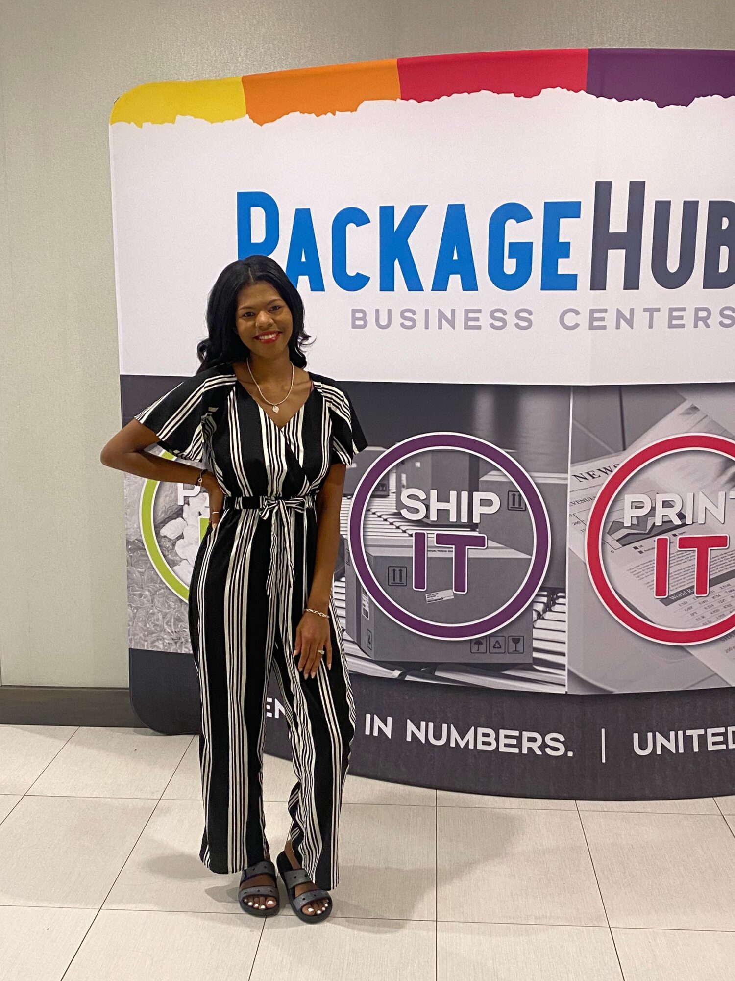 Woman in black and white striped dress standing in front of a colorful banner with text and logos.