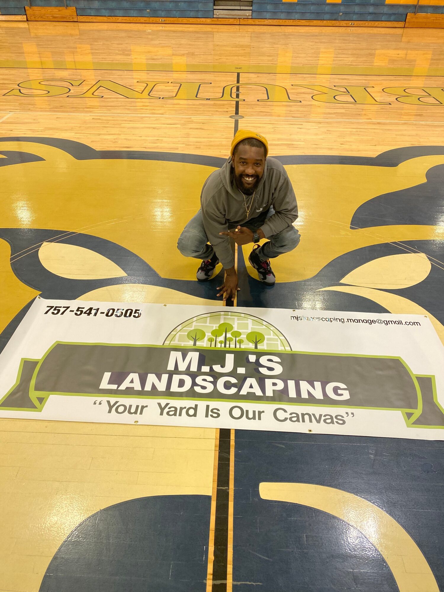 Person crouching next to a large MSU LANDSCAPING banner on a gym floor.