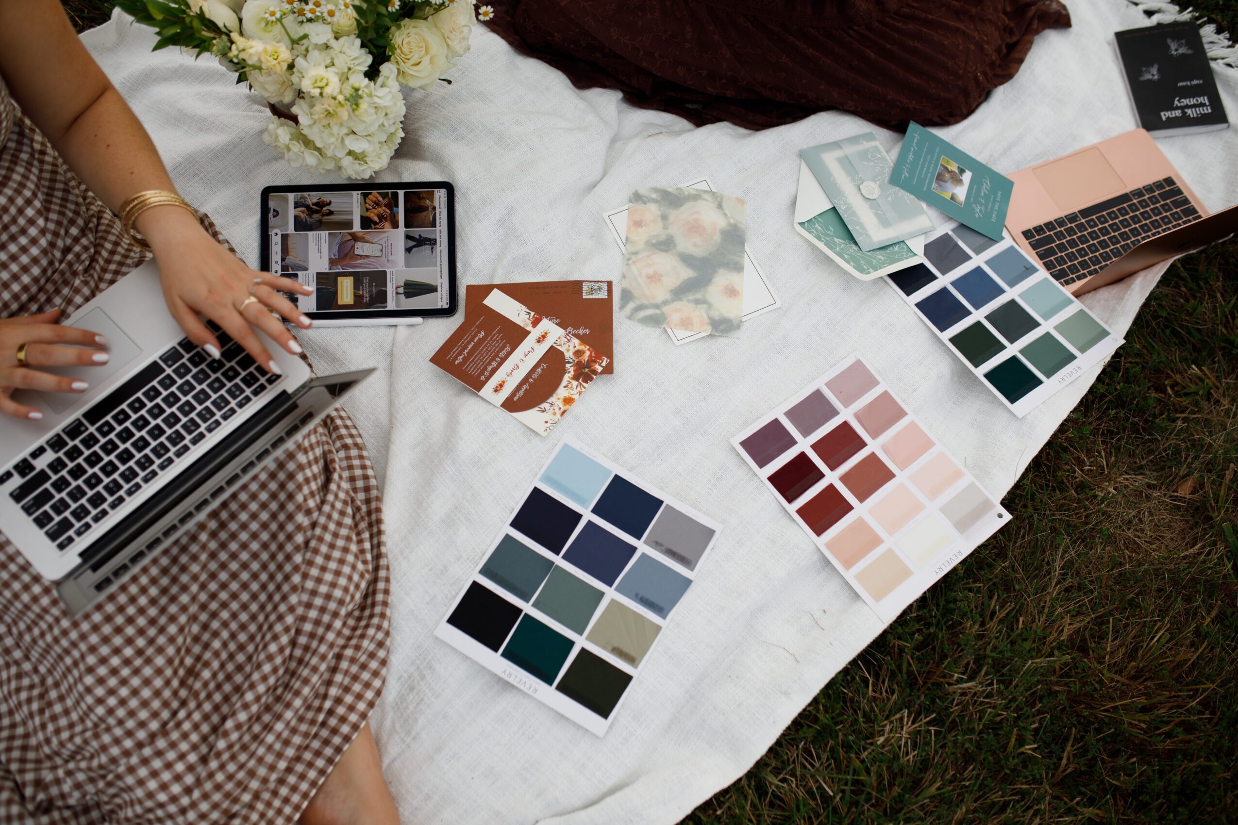 People working with laptops, color swatches, and printed materials on a white table outdoors.