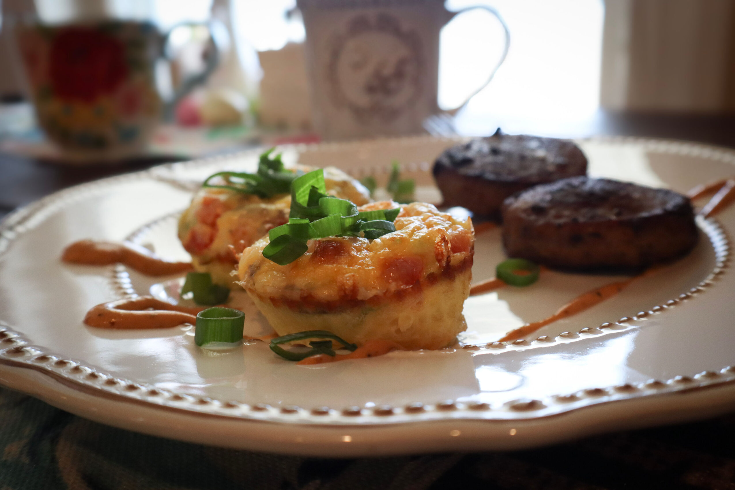 Two cooked meat patties and a piece of baked casserole with green onions on a decorative white plate, with a blurred background.