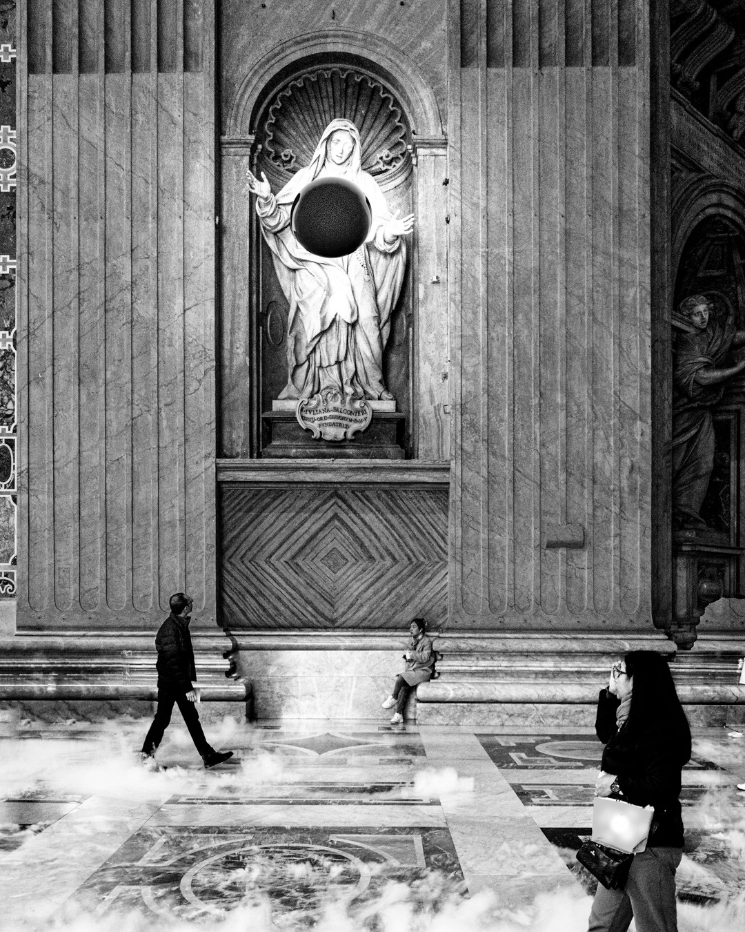 People walking inside a grand building with a large statue of a religious figure in a niche, black and white photo.