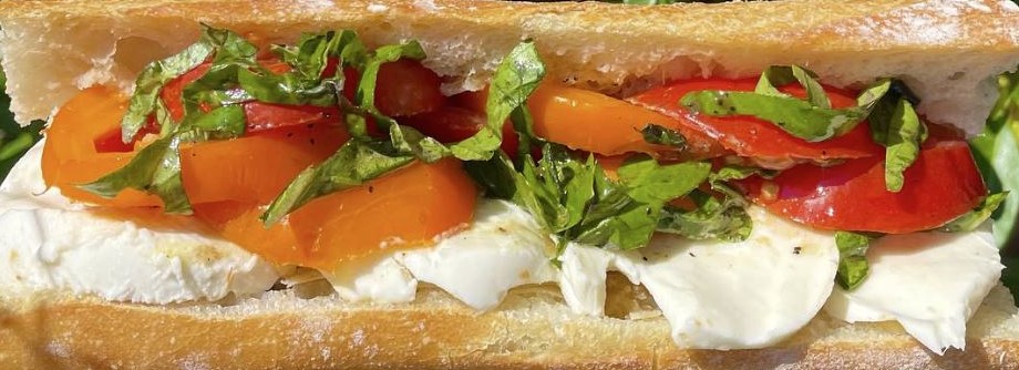 Sandwich with tomatoes, lettuce, and cheese on a baguette, close-up view.