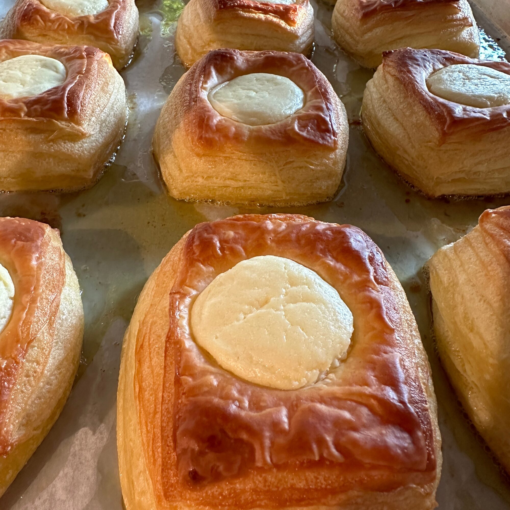Close-up of rectangular pastries with golden-brown crust and a dollop of white filling on top, arranged on a baking sheet.