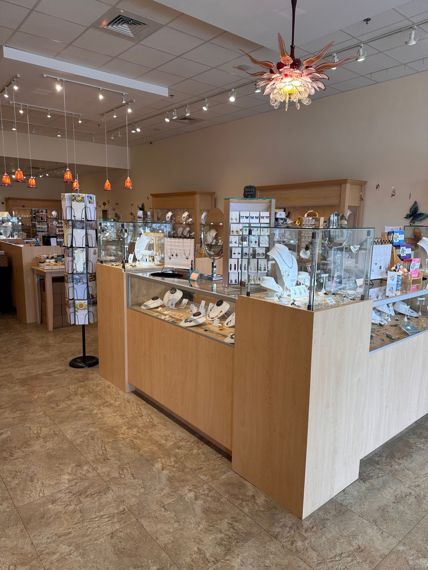 Wooden display counter with glass shelves holding various products inside a store, ceiling lights, and a tiled floor.