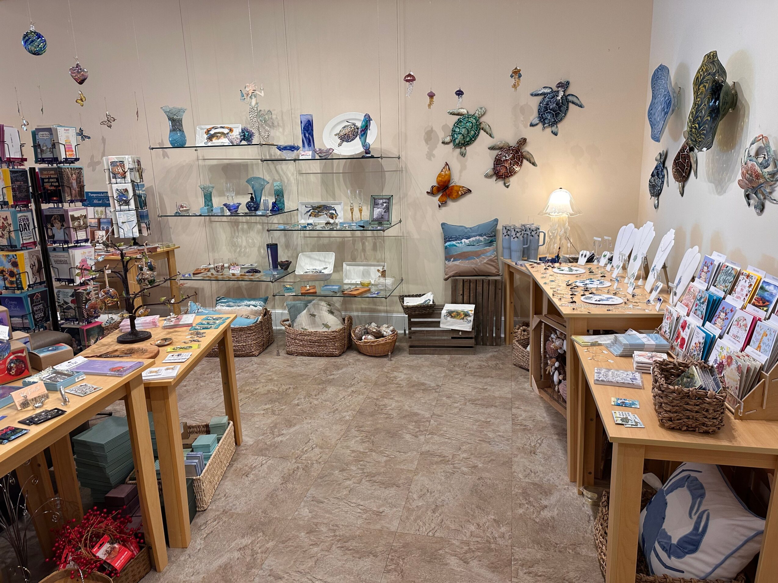 Store interior with glass shelves displaying blue and white decorative items, tables with books and crafts, and wall decorations.