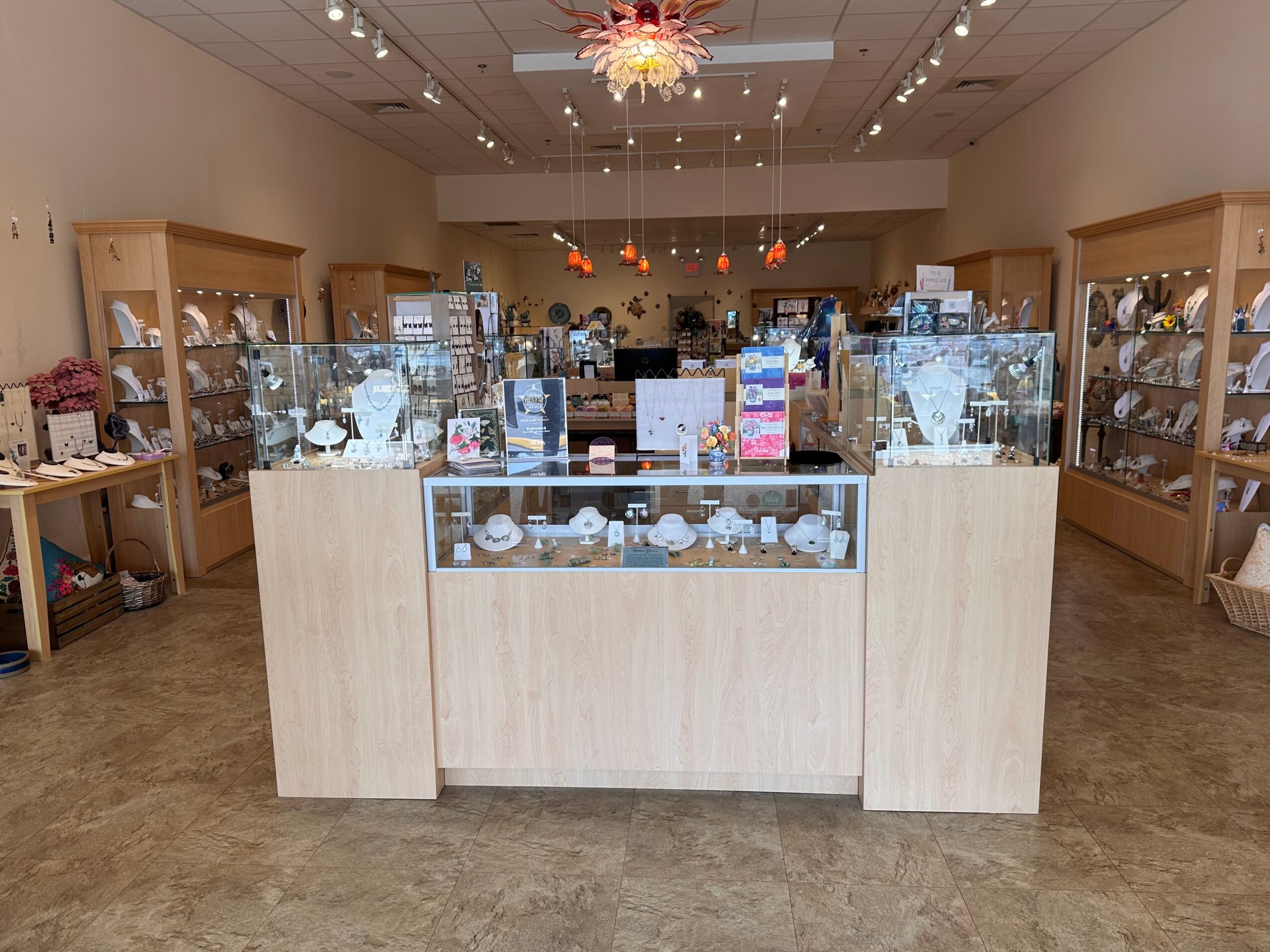 Jewelry display counter in a store with glass cases and wooden shelves, ceiling lights, and a chandelier.