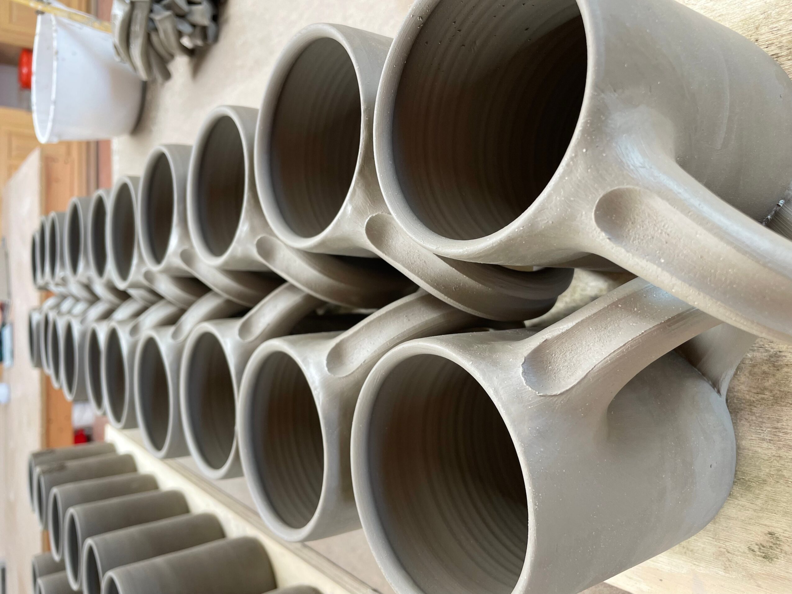 Multiple large gray ceramic mugs arranged in rows on a wooden surface, with a blurred background.