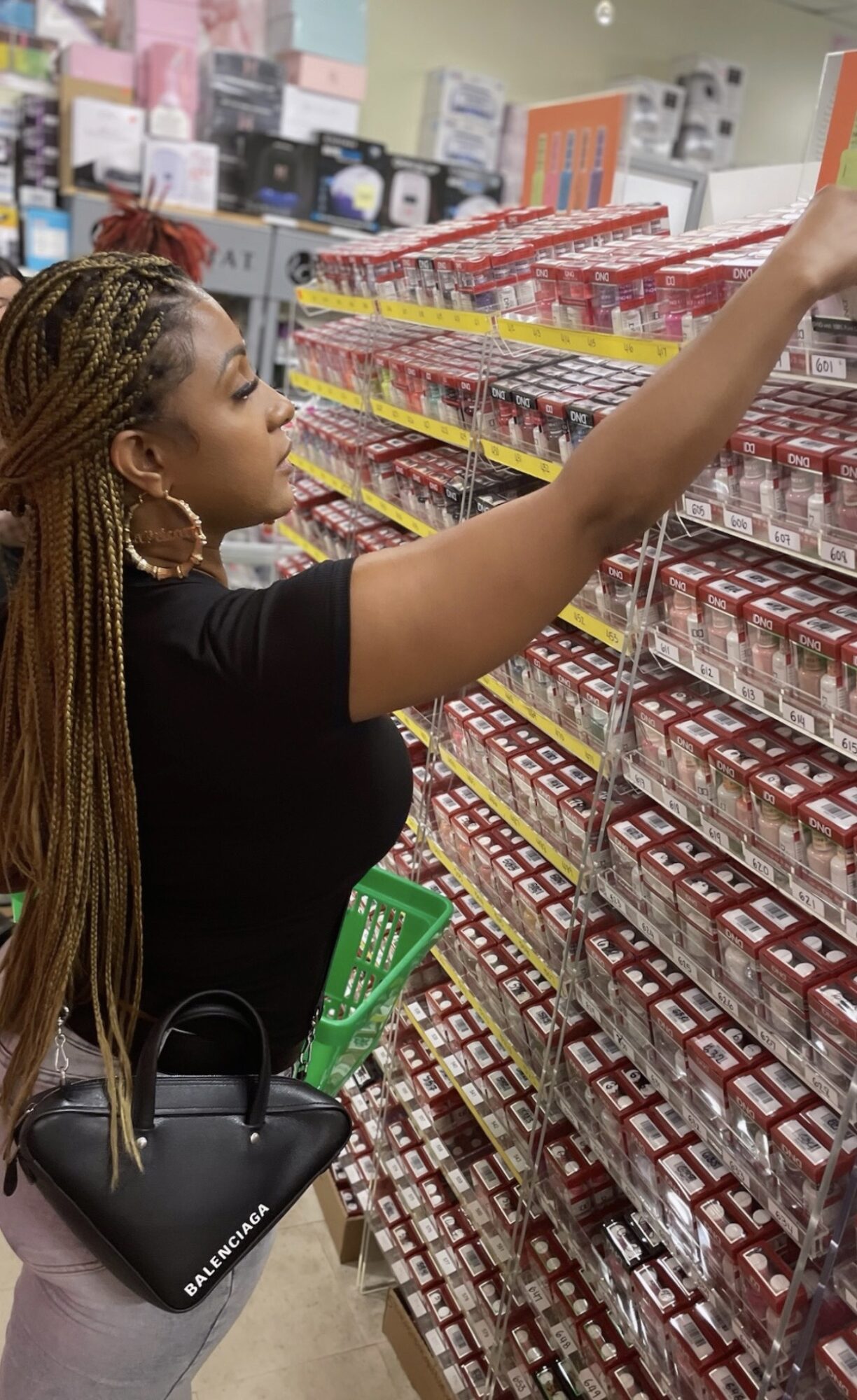Woman shopping in a store aisle, reaching for an item on the shelf, with a shopping basket and purse.