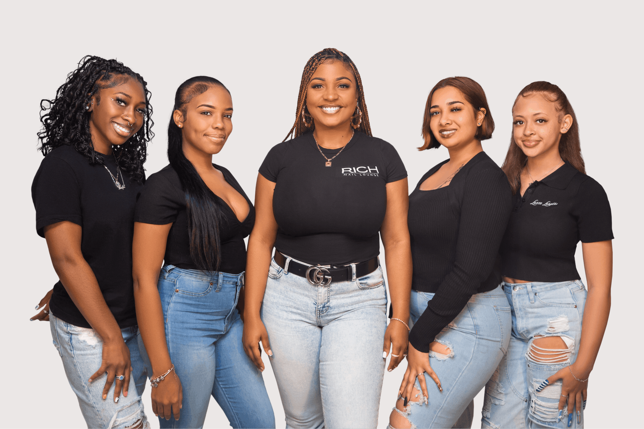 Group of five women standing together, smiling, wearing casual black tops and jeans, against a plain background.