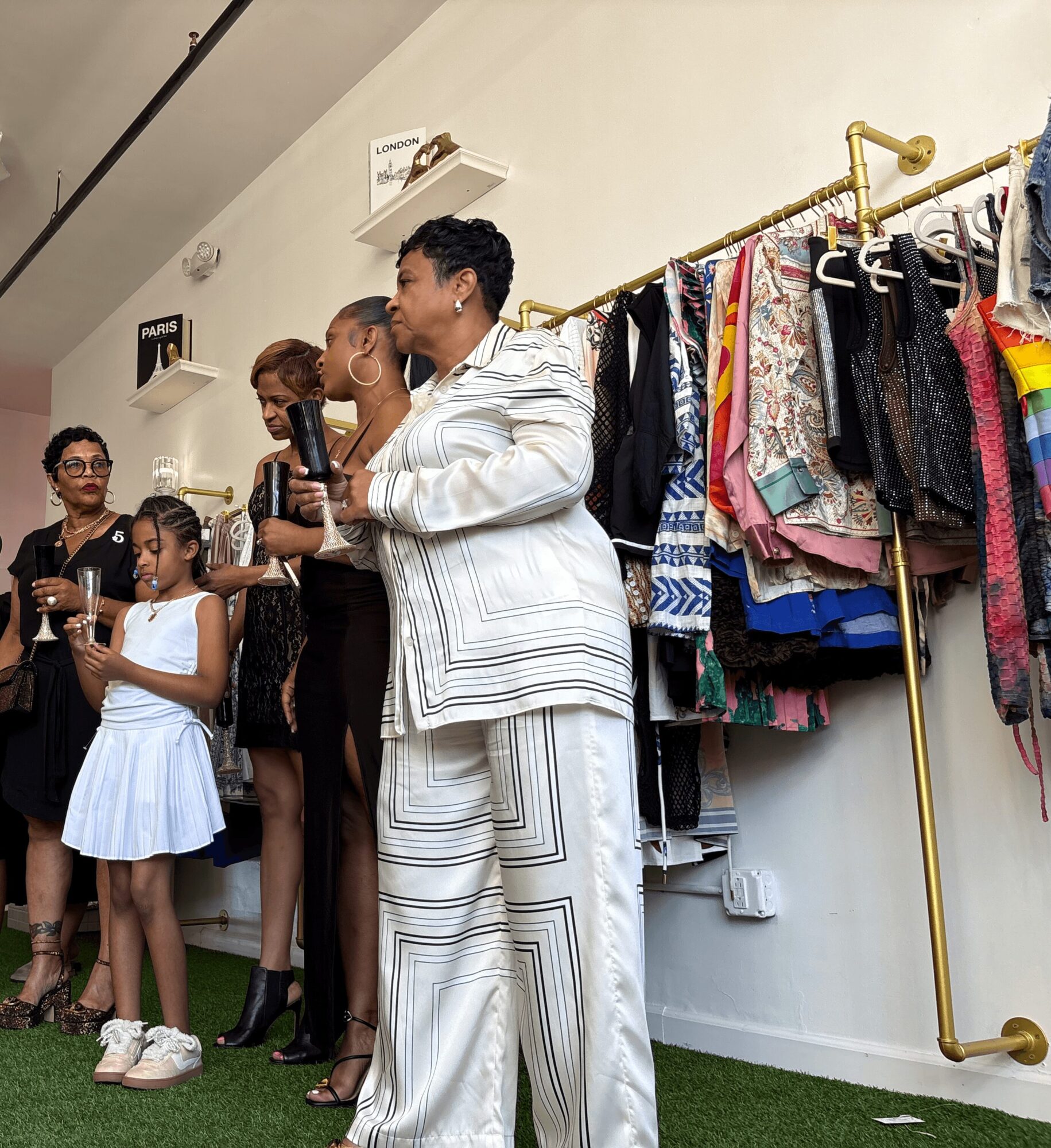 Group of people shopping for clothes, with a rack of colorful garments behind them, in a well-lit store.