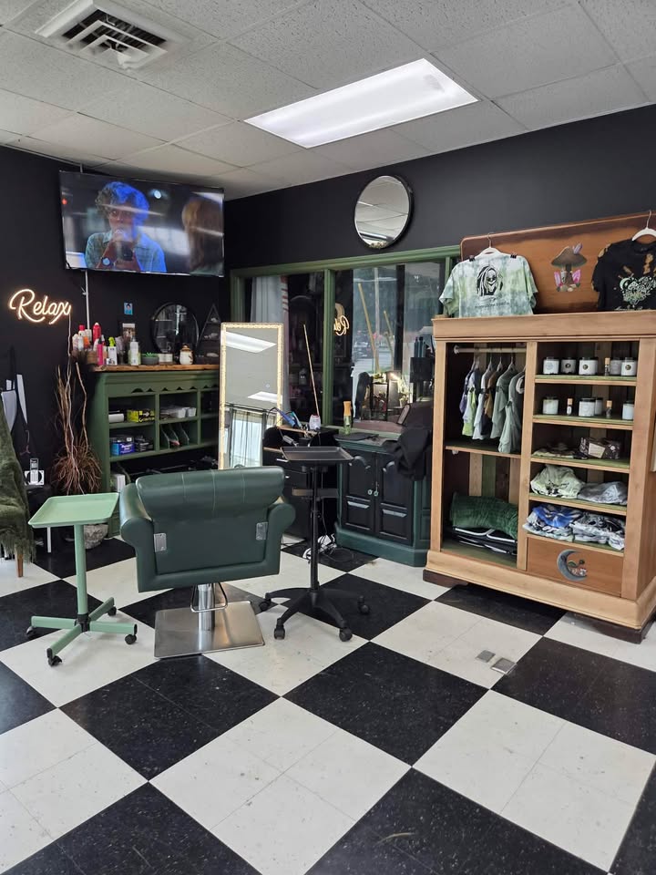 Barber shop interior with chair, mirror, shelves, and clothing display, black and white checkered floor, wall clock, and TV.