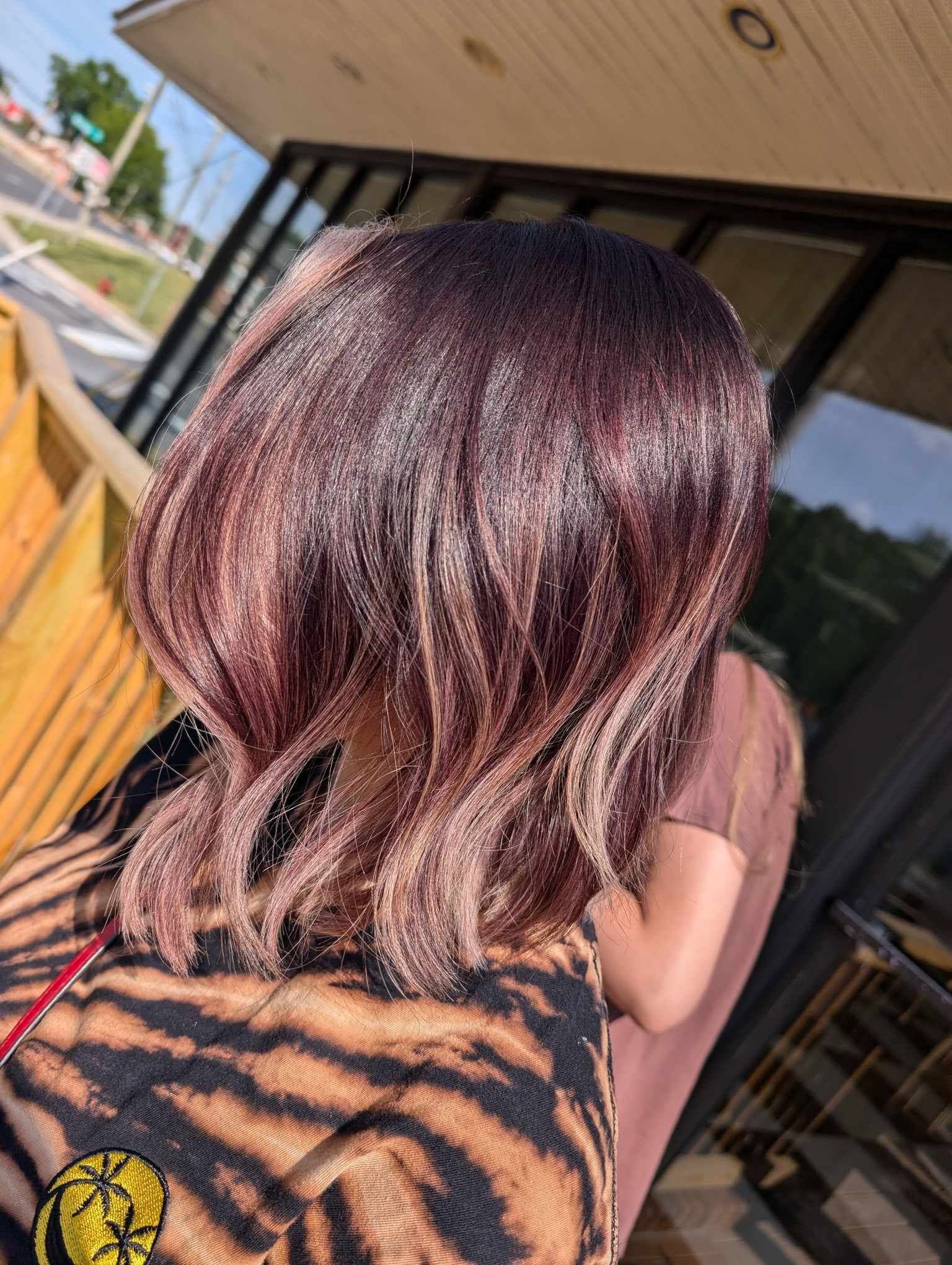Back view of a person with shoulder-length, wavy hair dyed in shades of pink and purple, standing outdoors near a building.