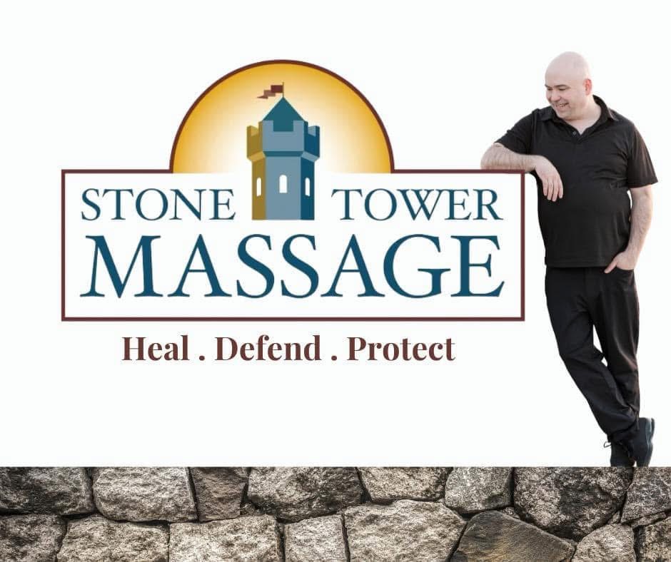 Man leaning on a sign for Stone Tower Massage with the tagline Heal, Defend, Protect, and a stone wall at the bottom.