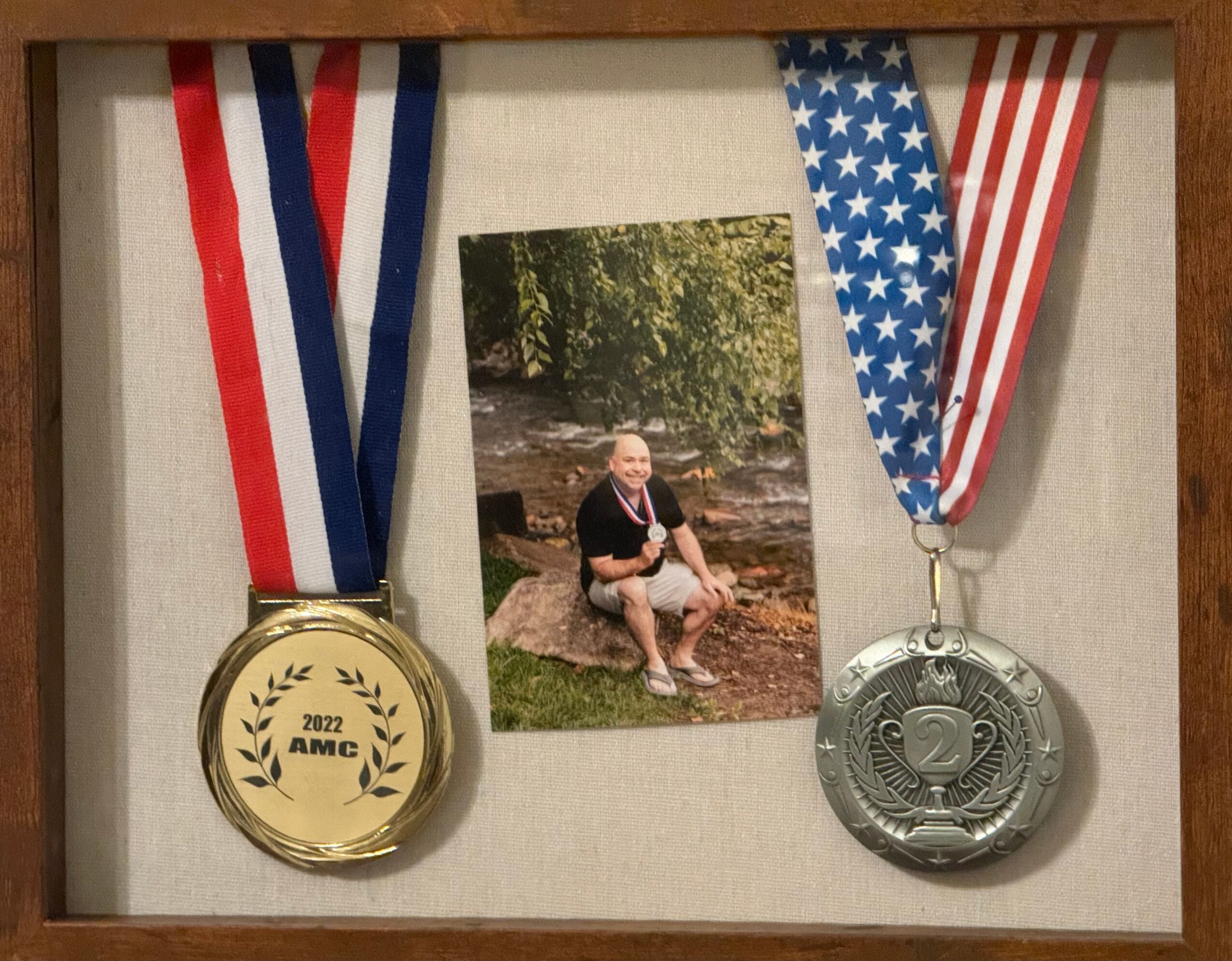 Photo of a person sitting on a rock by a stream, framed with two medals on ribbons, one gold and one silver.