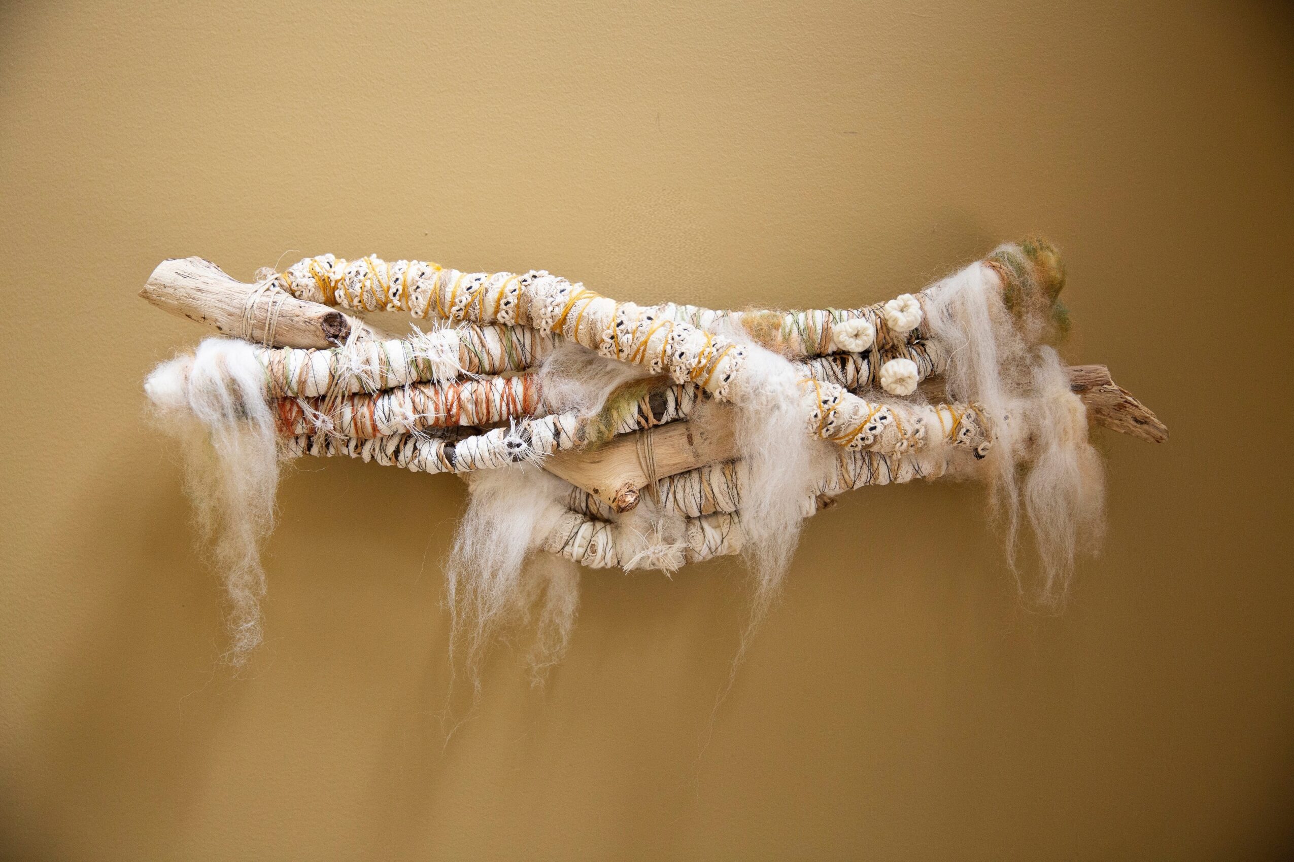 Three textured, white and beige fabric-covered branches with hanging white fibers against a plain beige background.