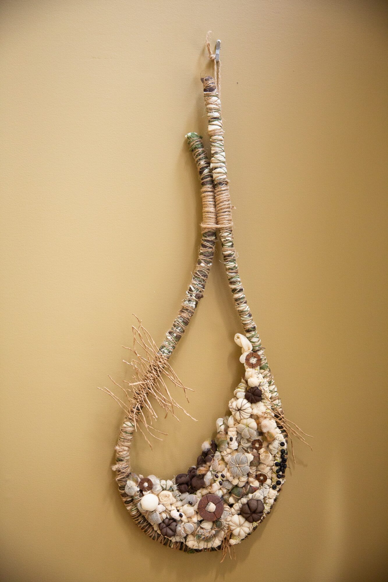 Decorative hanging ornament made of shells, beads, and natural materials, shaped like a teardrop, against a plain background.
