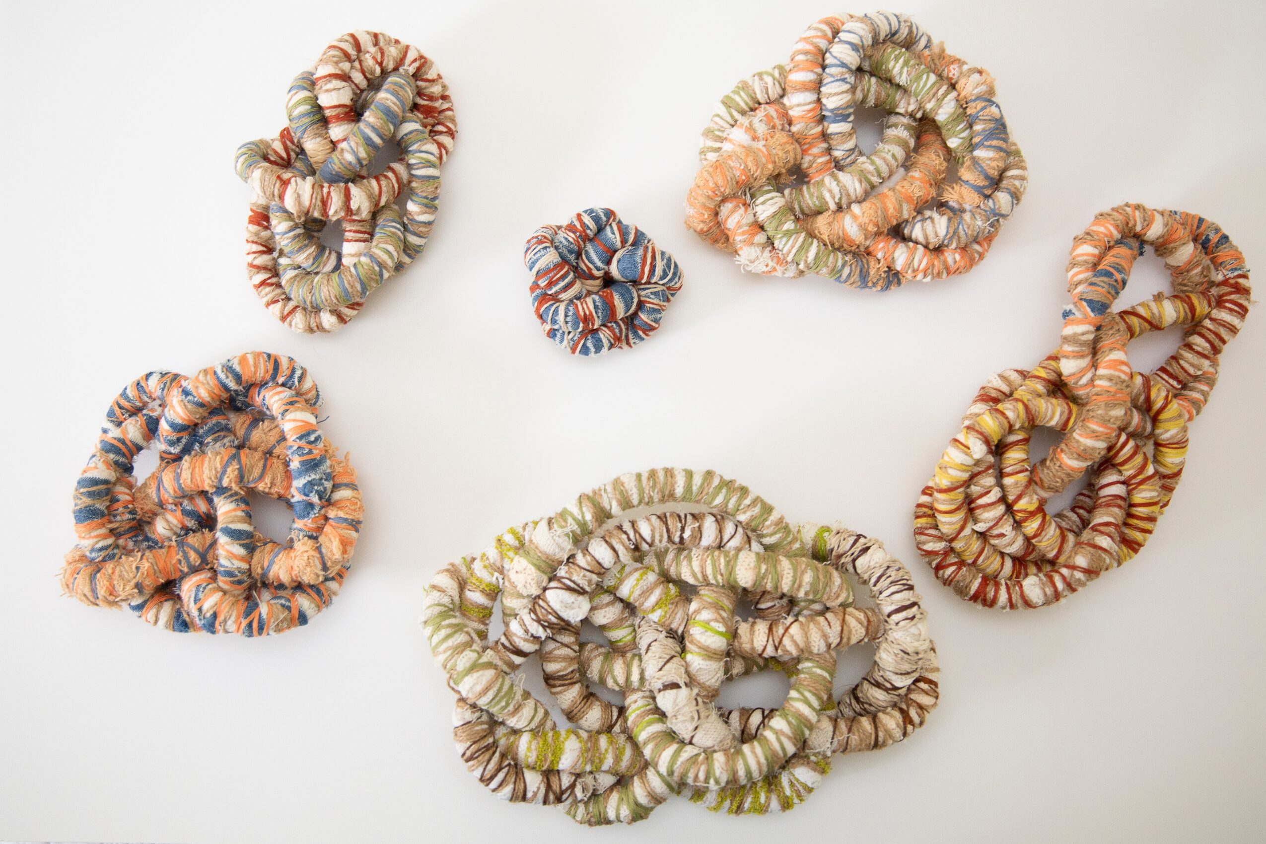 Six fabric scrunchies in various colors and patterns arranged on a white background.