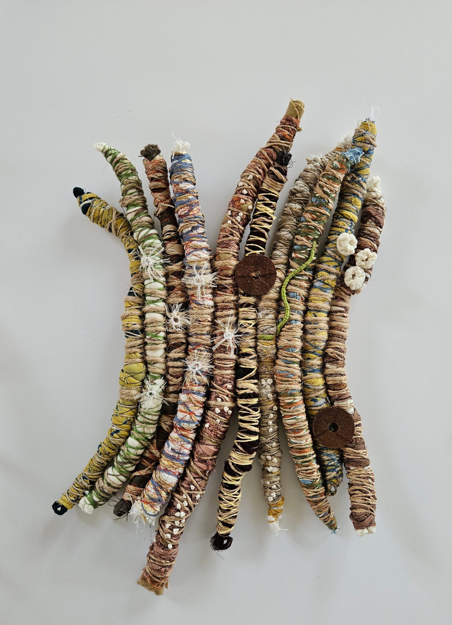 Multiple colorful, textured fabric or yarn strips arranged in a cluster on a plain background.