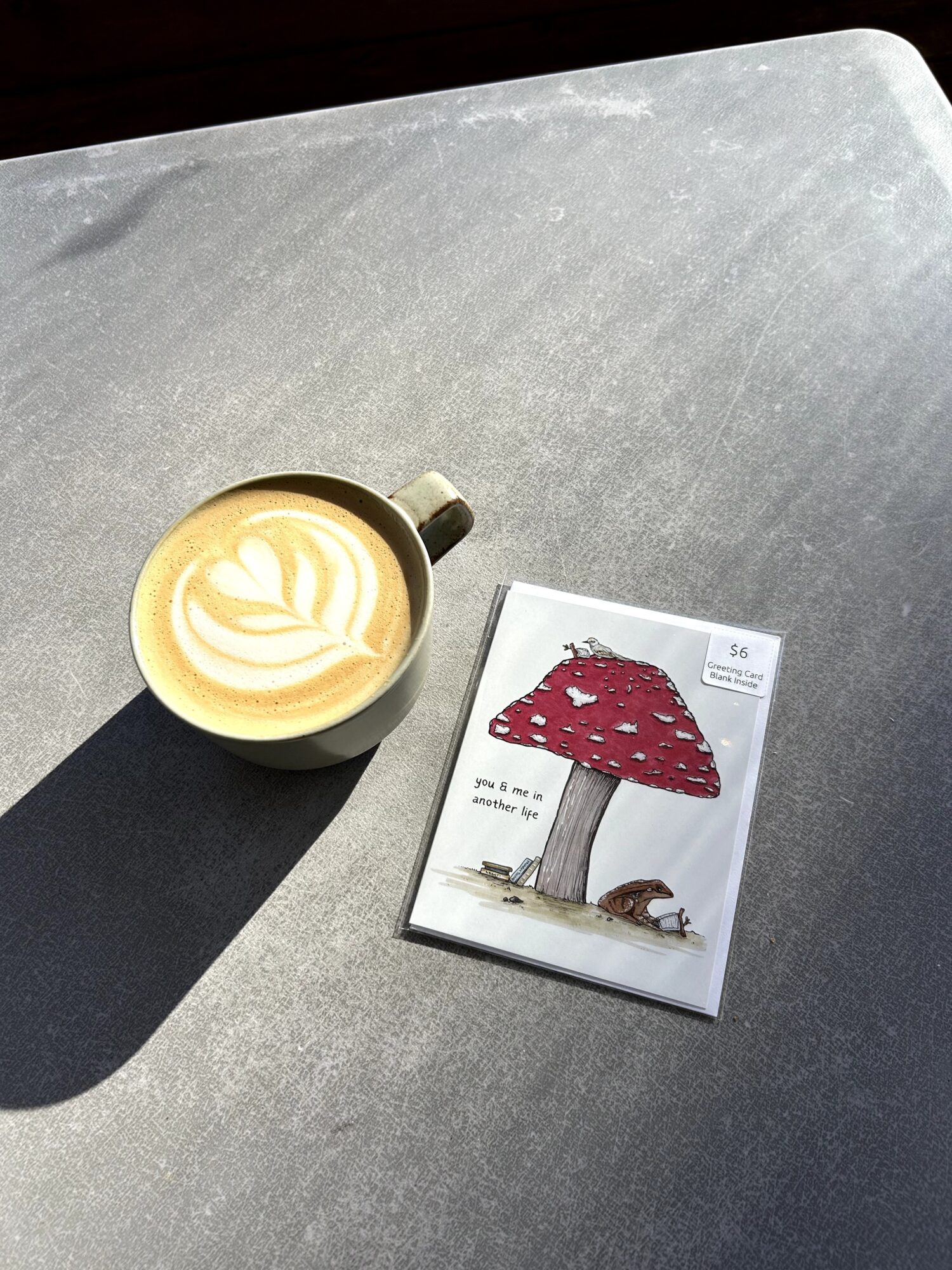 A cup of latte with latte art and a small book with a red mushroom illustration on a gray surface.
