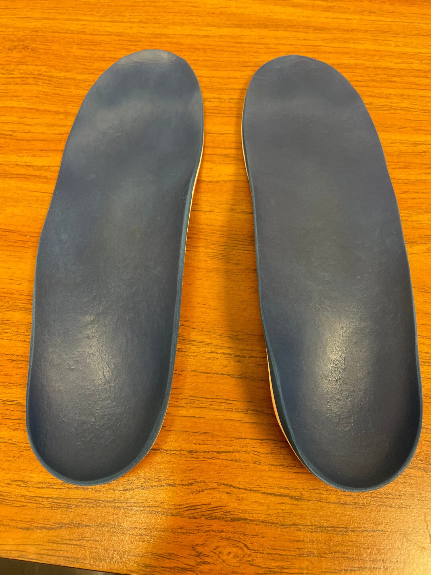 Two shoe insoles placed side by side on a wooden surface, showing the top view.
