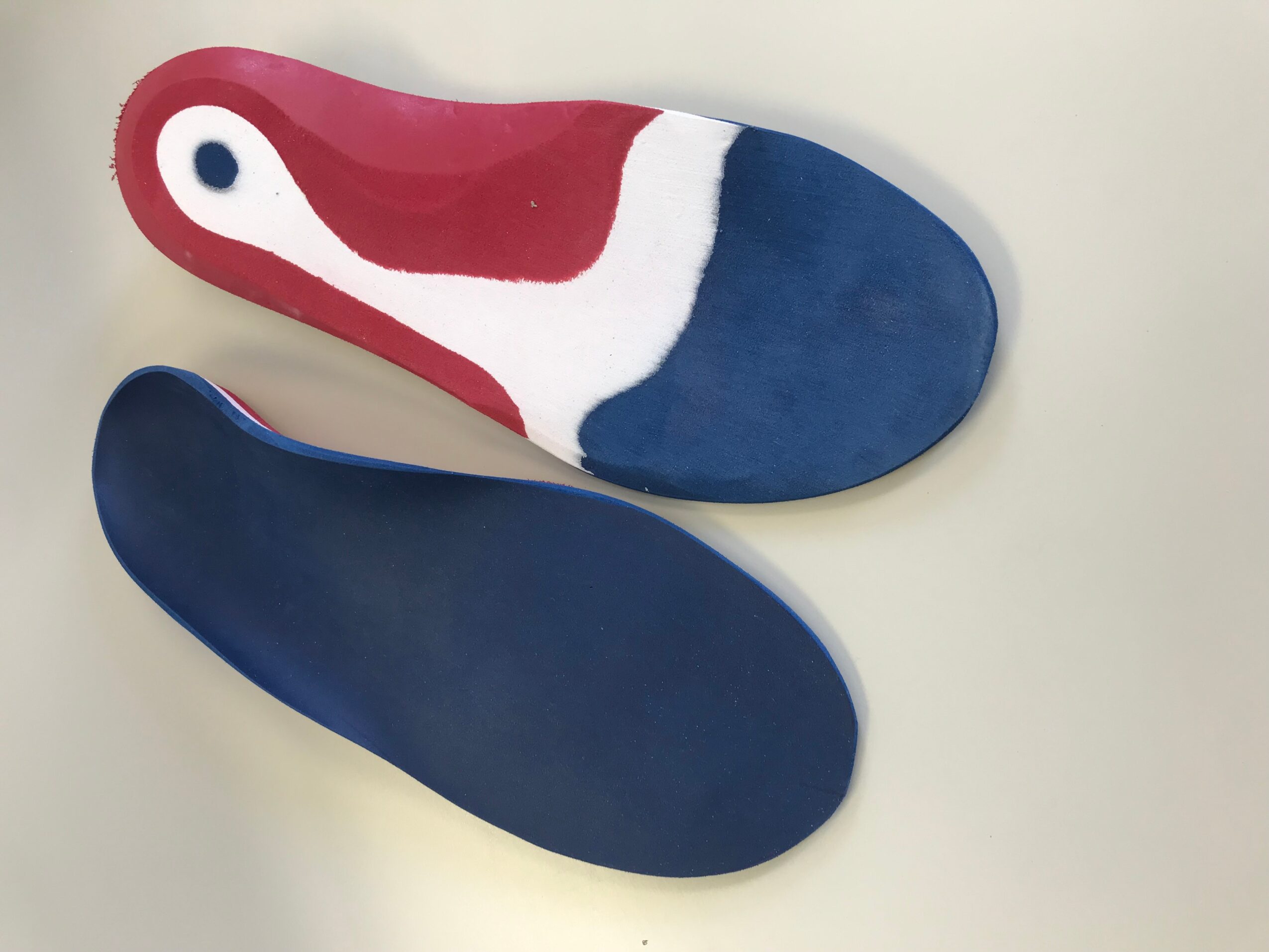Two shoe insoles, one with red, white, and blue colors, and the other plain blue, placed on a white surface.