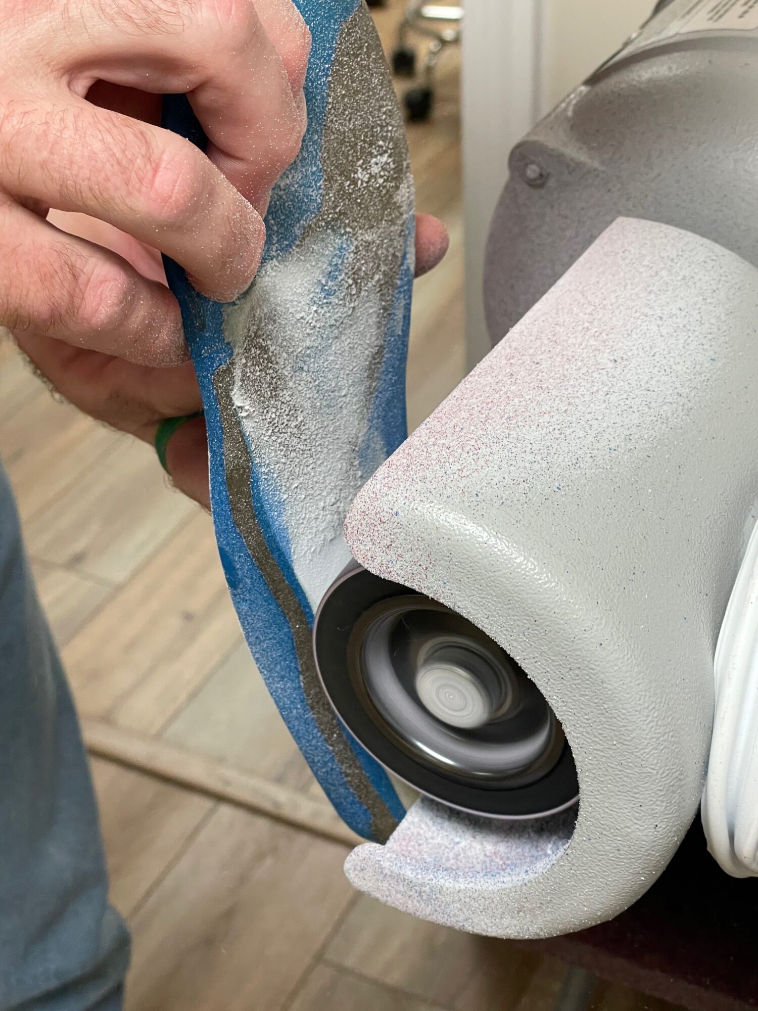 Person holding a blue cloth cleaning a speaker with a white surface, in a room with wooden flooring.