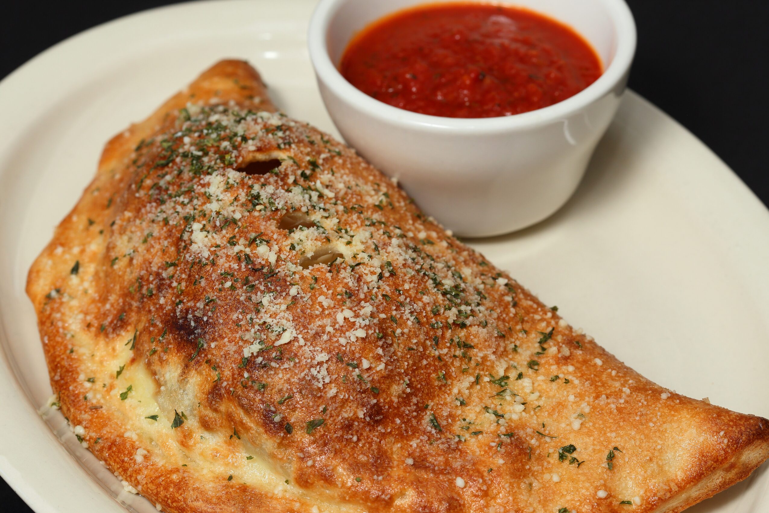Fried fish fillet with seasoning, served with a bowl of red dipping sauce on a white plate.