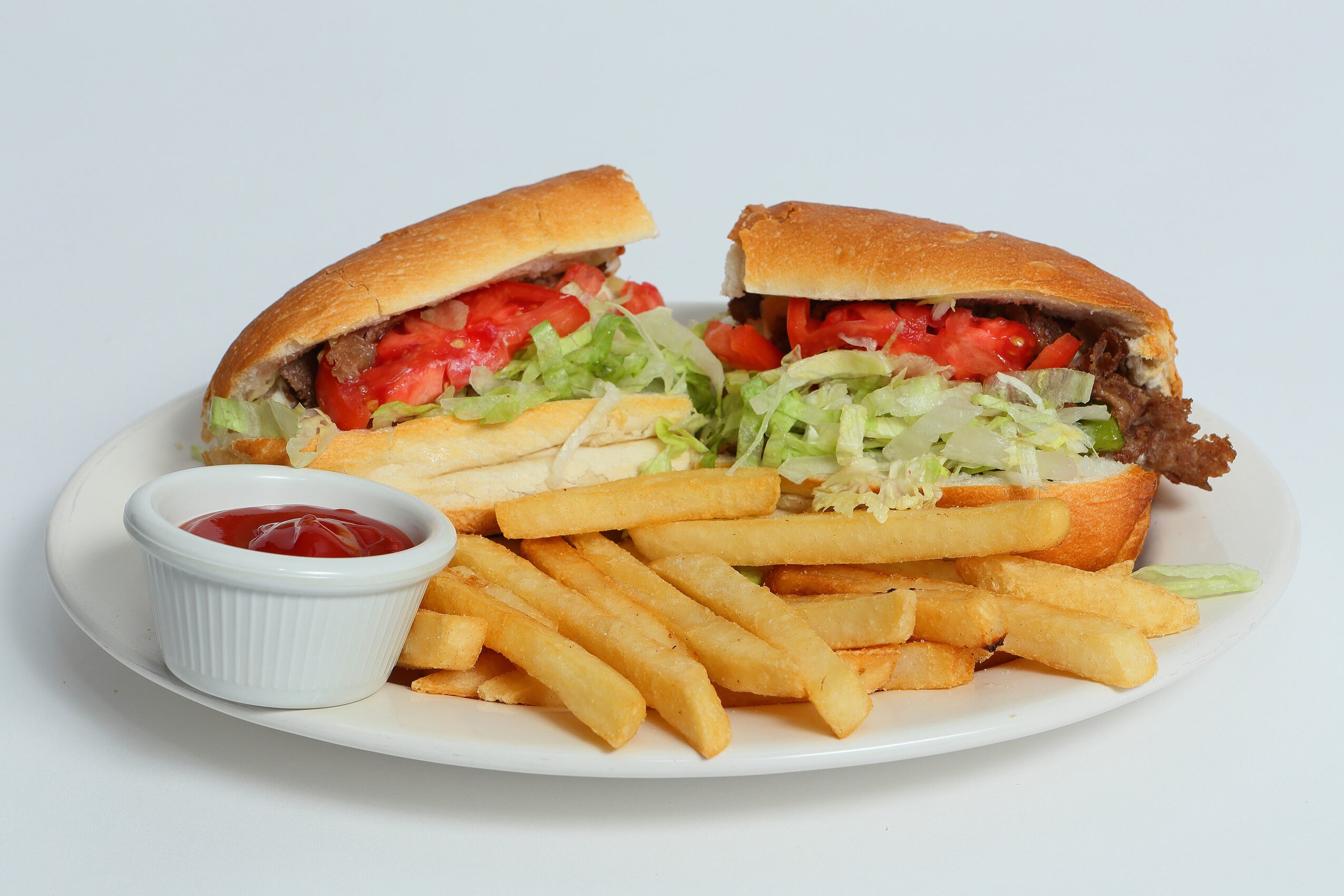 Hamburger with lettuce, tomato, cheese, and beef patty, served with French fries and ketchup on a white plate.