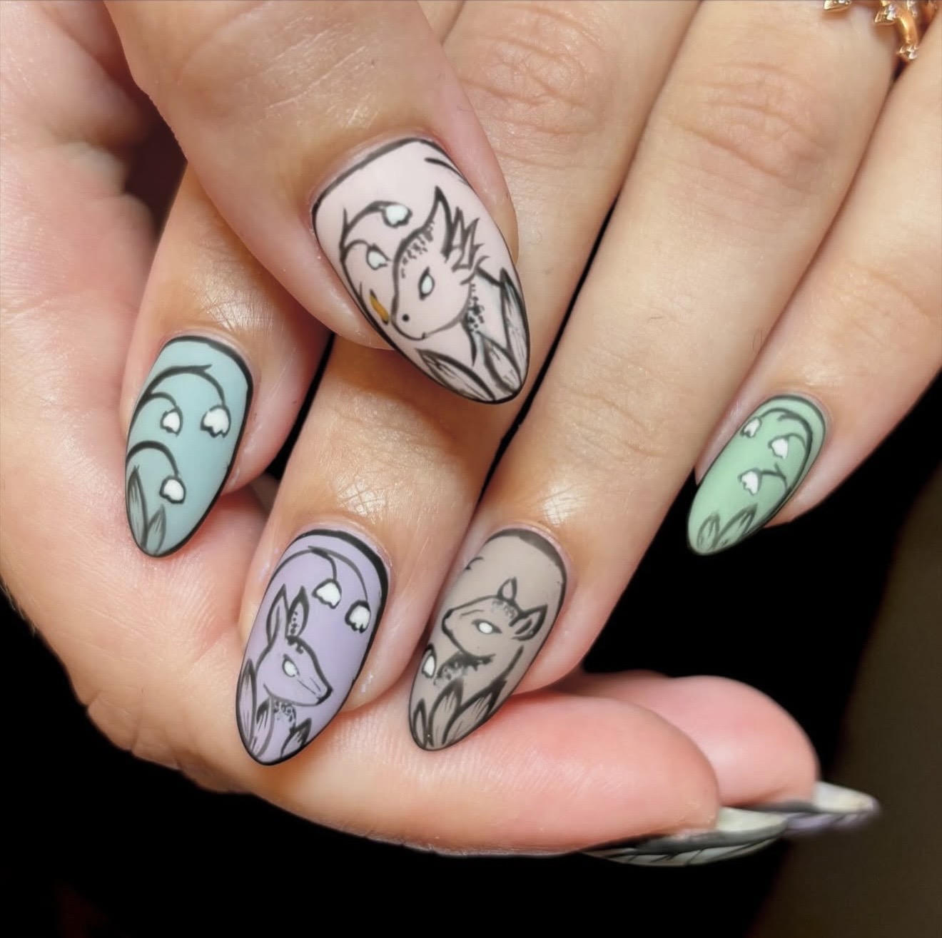 Hand with five nails painted with cartoon animal designs, including a unicorn, wolf, and other creatures, on a light background.